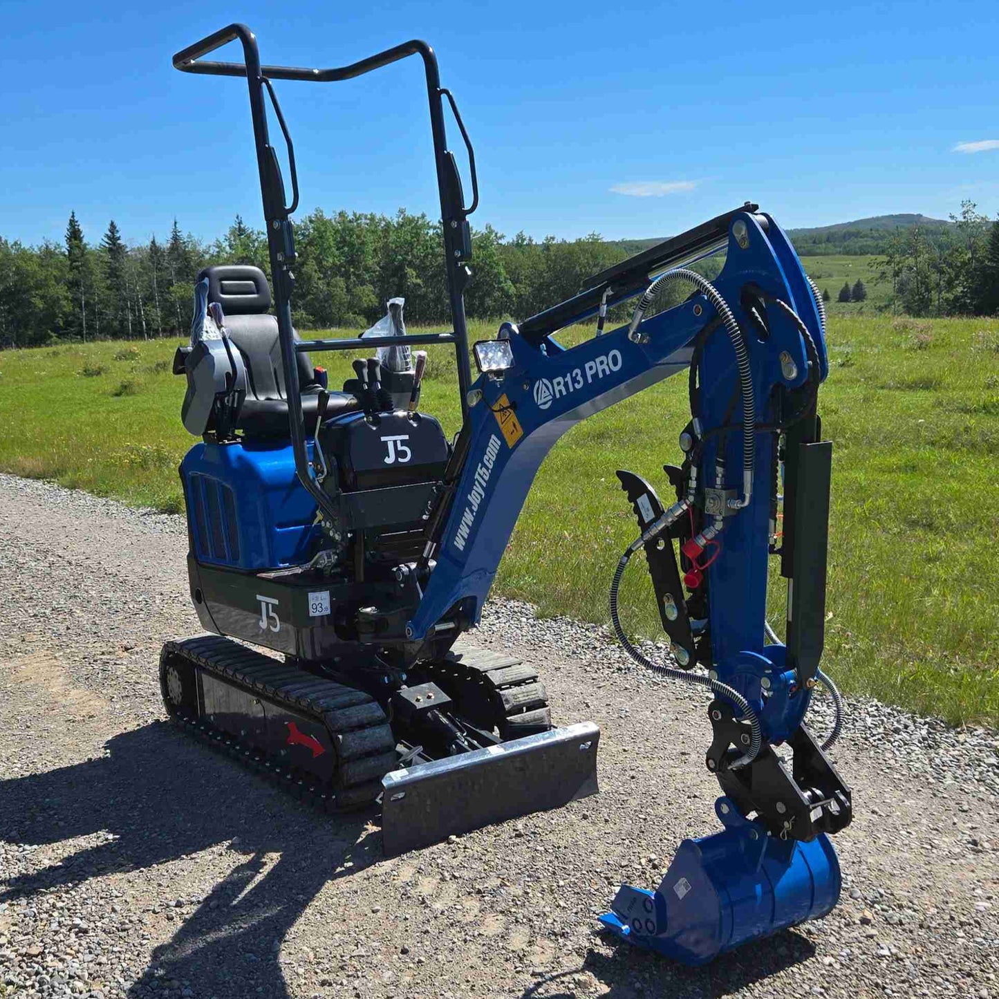 Rippa R13 mini excavator for sale by JoyT5 on a gravel road with green fields and trees in the background
