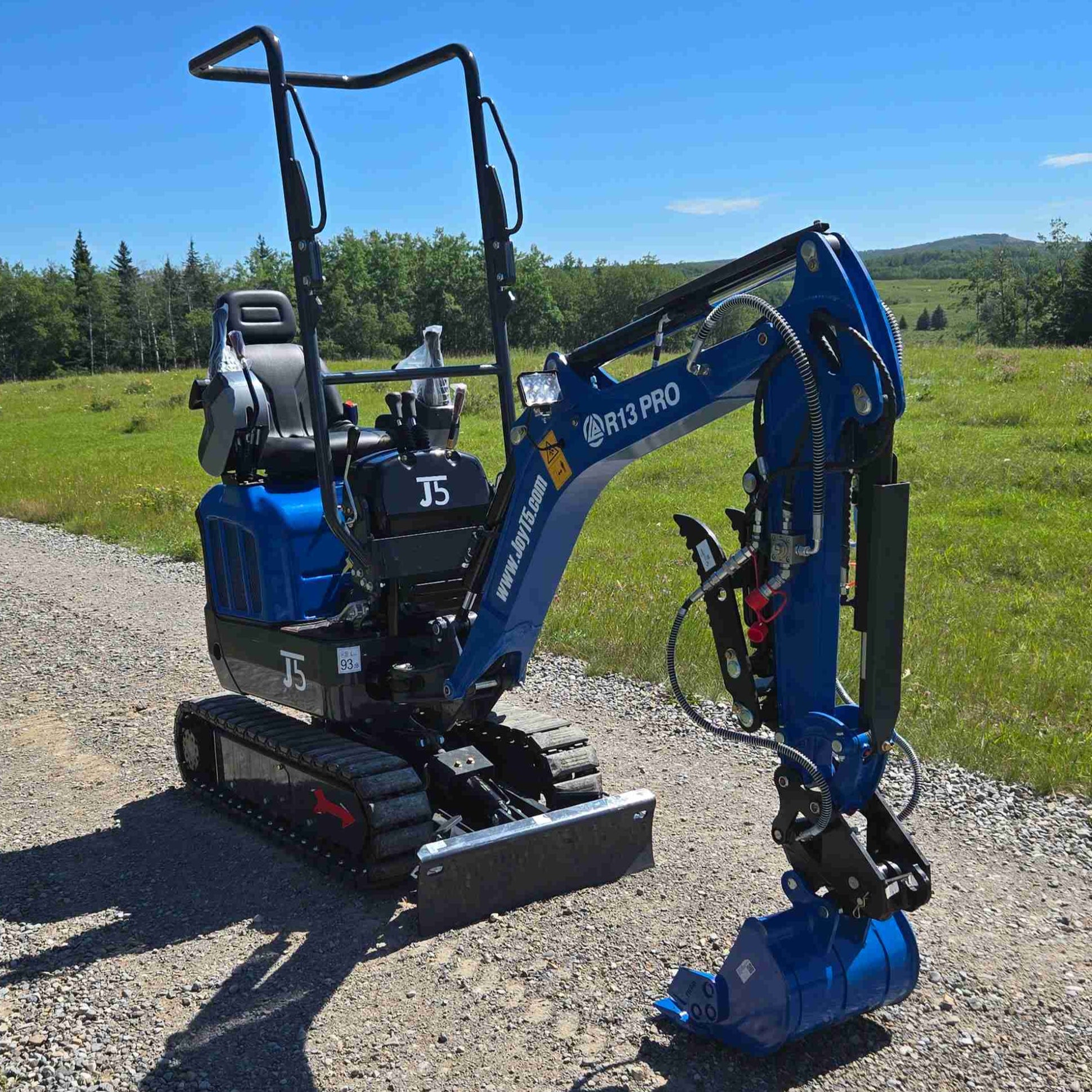 Rippa R13 mini excavator for sale by JoyT5 on a gravel road with green fields and trees in the background