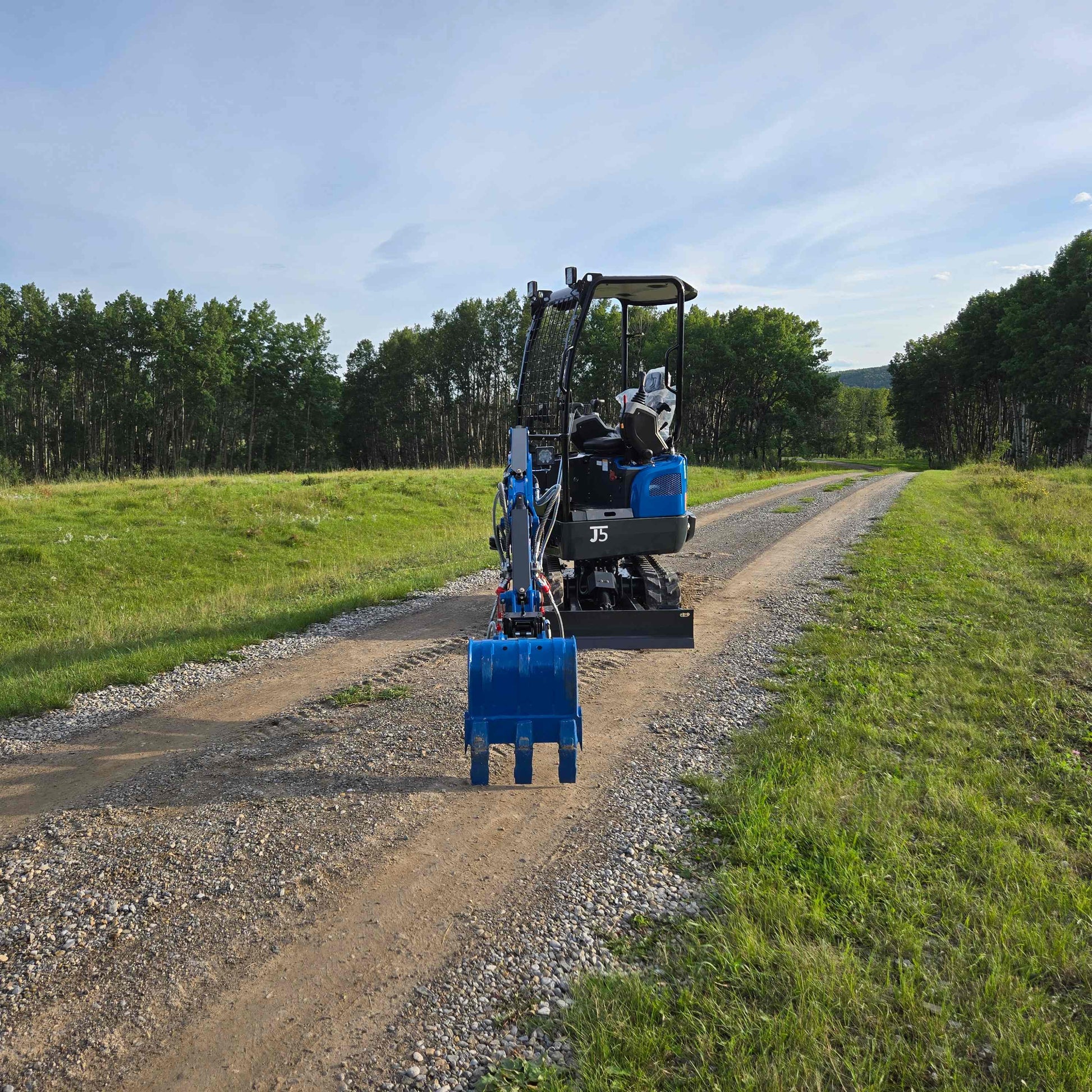  Rippa R18 Mini Excavator for sale JoyT5 | rear angle view on a gravel road with blue digging bucket in a natural green environment
