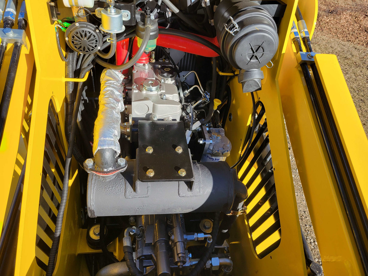 Close up of engine compartment on diesel tracked mini skid steer 25 HP loader in Canada showing detailed hydraulic system and durable engine design for construction use

