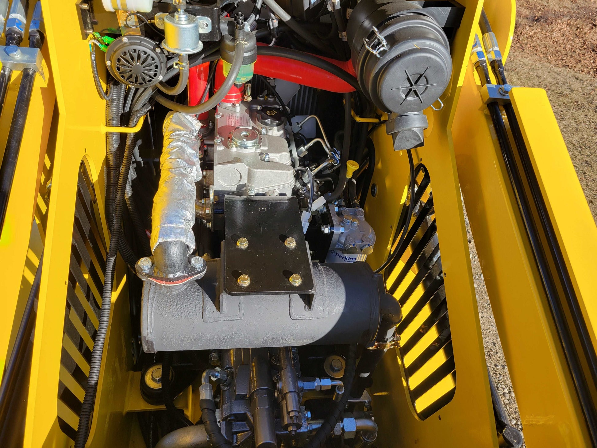 Close up of engine compartment on diesel tracked mini skid steer 25 HP loader in Canada showing detailed hydraulic system and durable engine design for construction use

