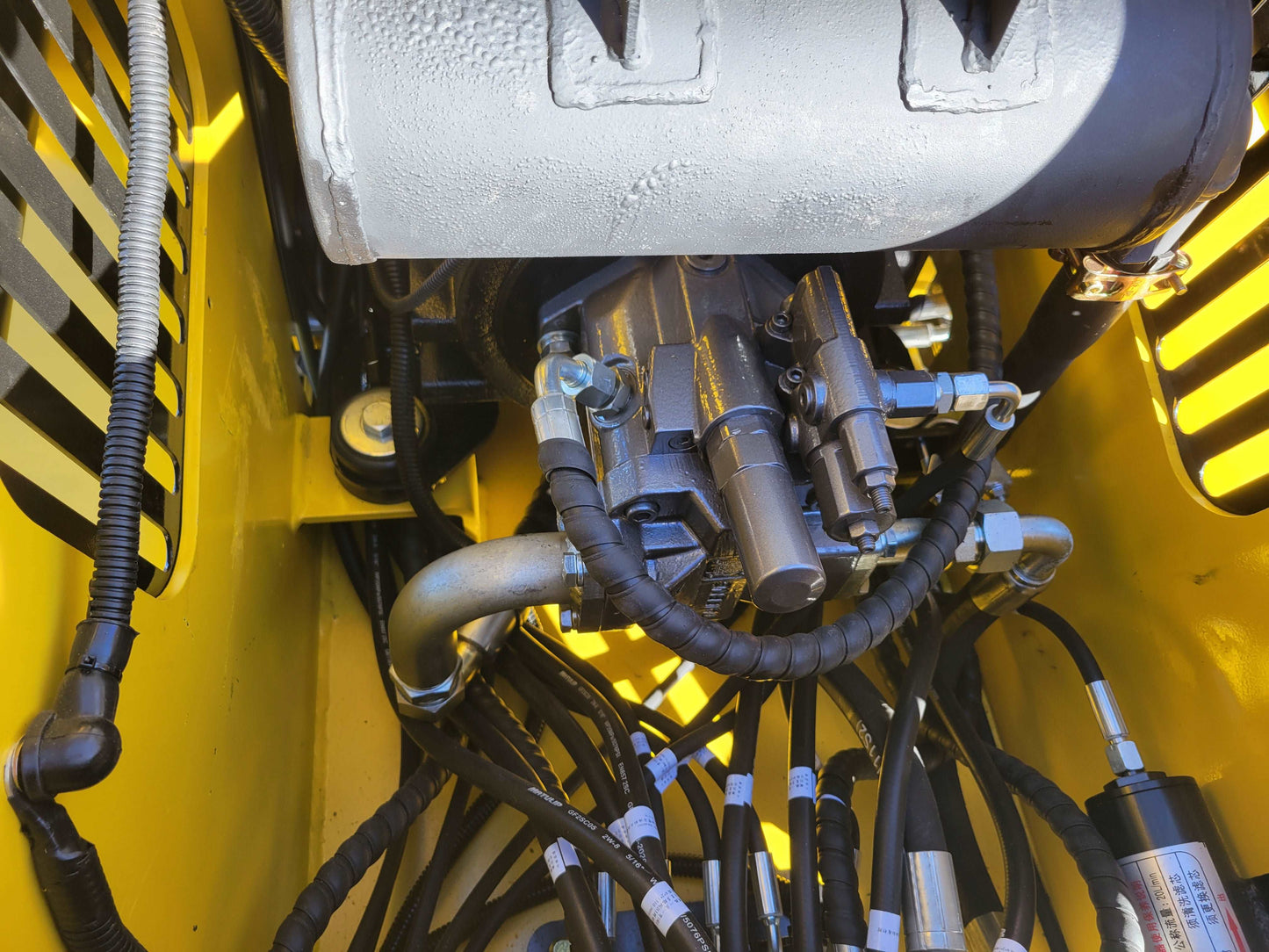 Close up of hydraulic valve and connector lines inside diesel tracked mini skid steer 25 HP loader in Canada showing detailed hydraulic control system for construction and landscaping work


