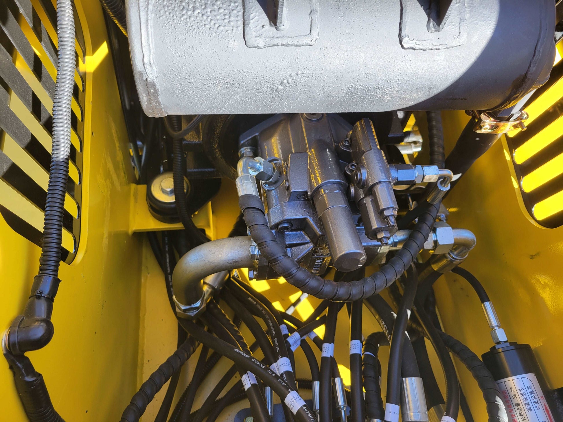 Close up of hydraulic valve and connector lines inside diesel tracked mini skid steer 25 HP loader in Canada showing detailed hydraulic control system for construction and landscaping work


