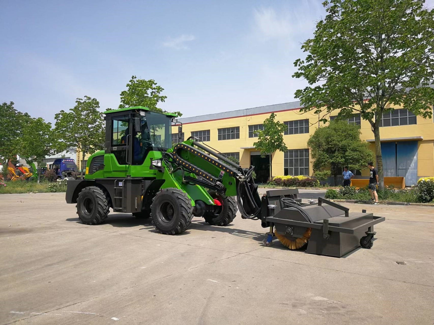 Green wheel loader equipped with road sweeper attachment for street cleaning and construction site maintenance