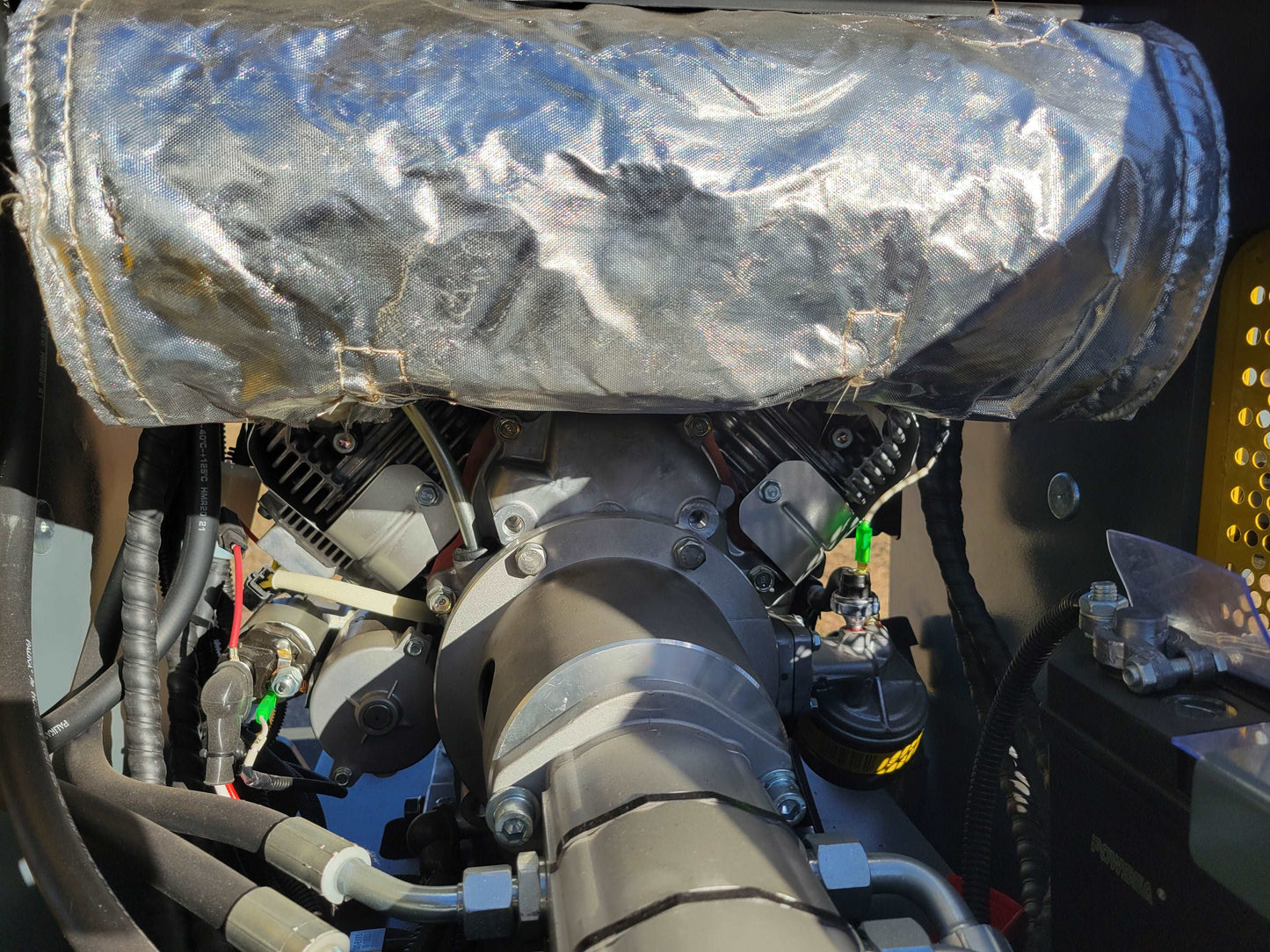Close-up view of JoyT5 JT5SSTM3 mini skid steer loader engine with protective heat shield and connected hydraulic components