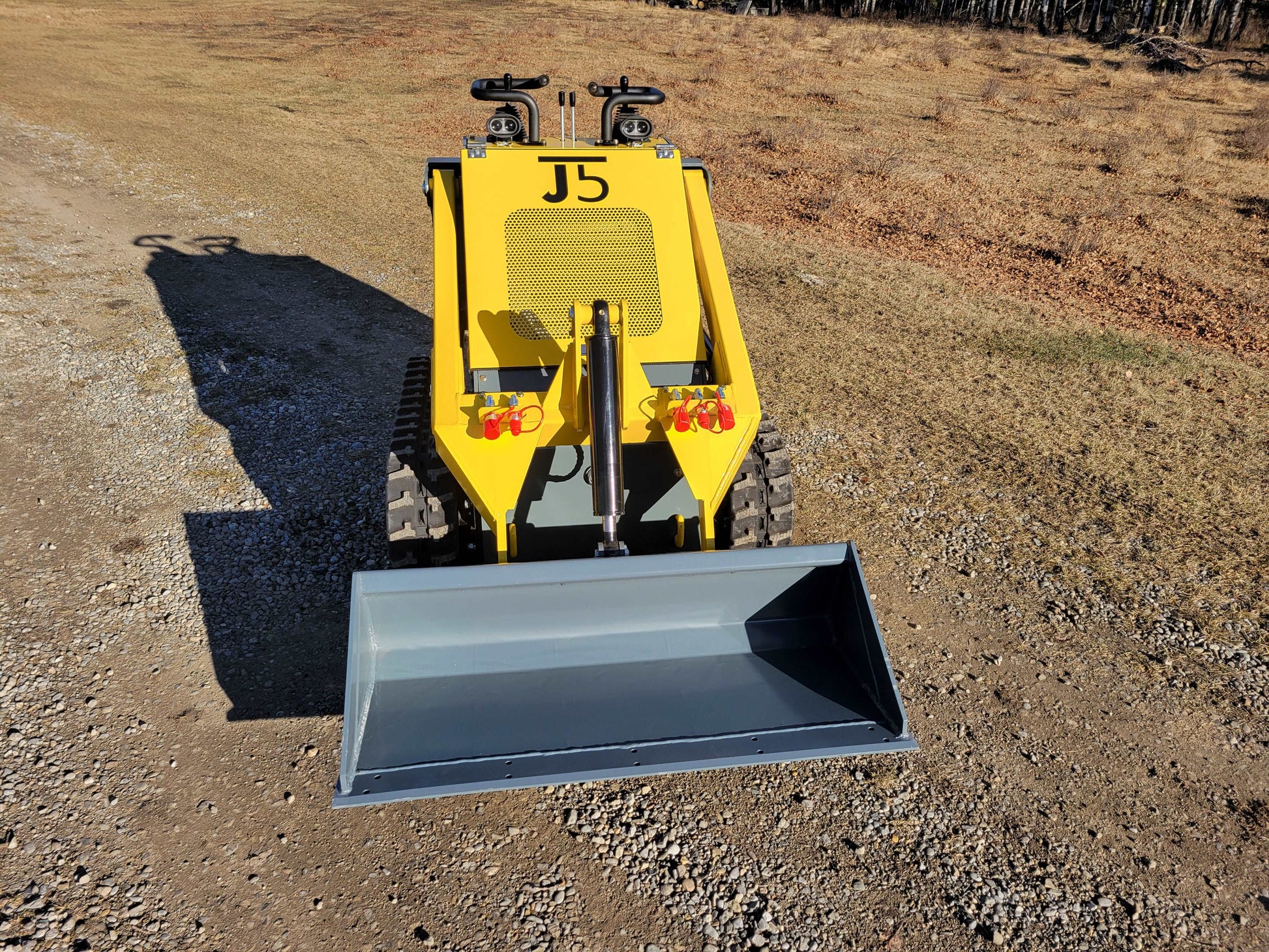 JoyT5 JT5SSTM3 mini tracked skid steer shown from front with wide bucket for landscaping and construction work on gravel surface in Canada
