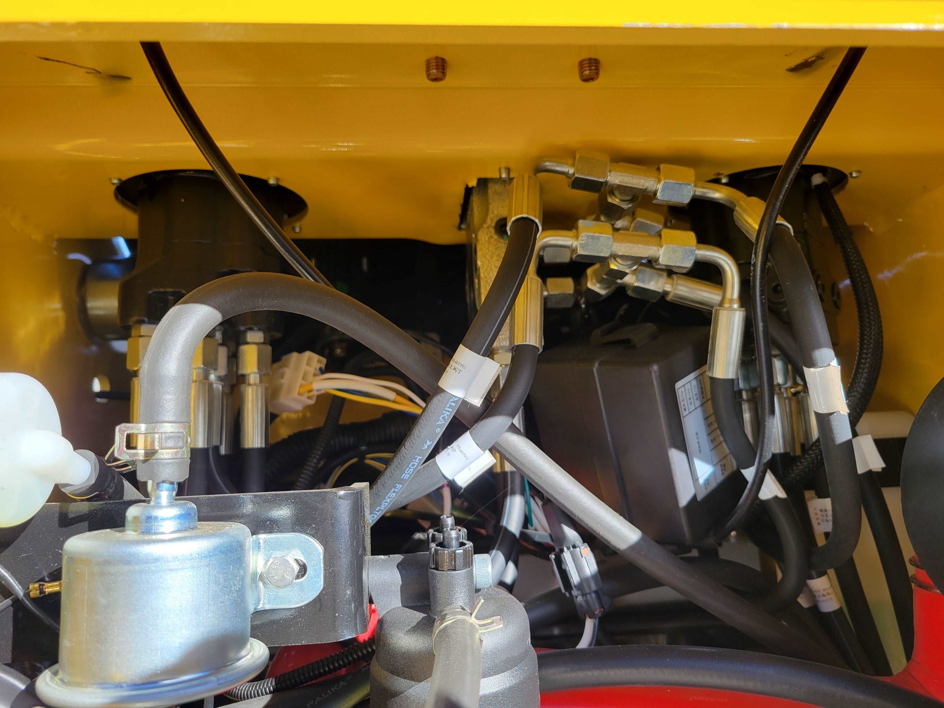 Hydraulic hose connections and pump components inside JoyT5 JT5SSTM4 mini skid steer with detailed wiring and fittings.