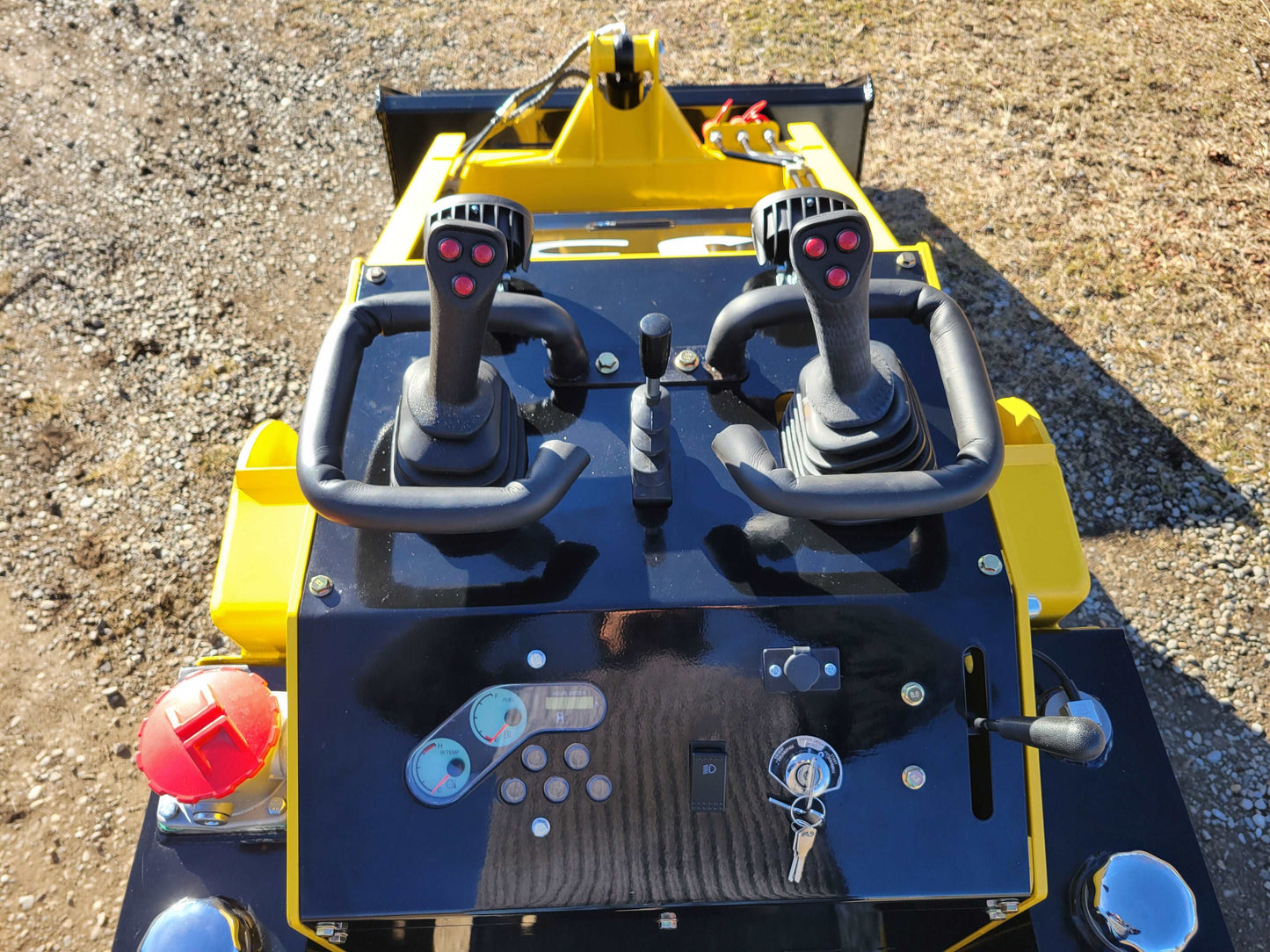 Close-up of JoyT5 JT5SSTM4 mini skid steer loader dashboard with dual joystick controls, ignition key, and machine control switches.