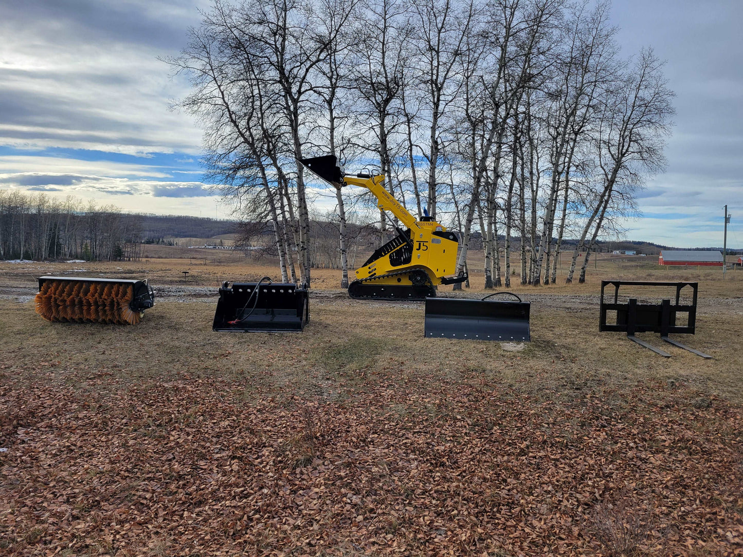 JoyT5 JT5SSTM4 mini skid steer loader with bucket, snow blade, pallet forks, and brush sweeper attachments displayed outdoors.