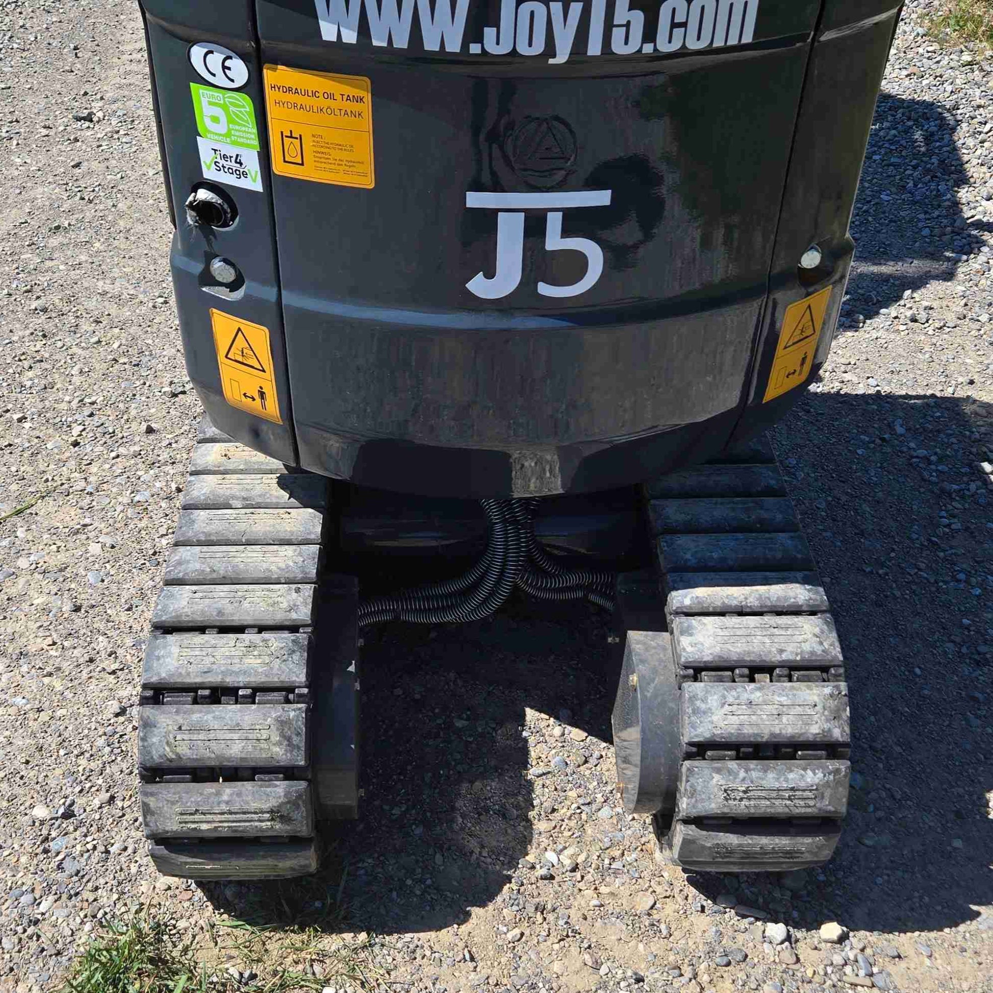 Rear undercarriage view of JoyT5 mini excavator showing durable rubber tracks, protected hydraulic lines and J5 branding, designed for compact construction, landscaping and utility projects across Canada
