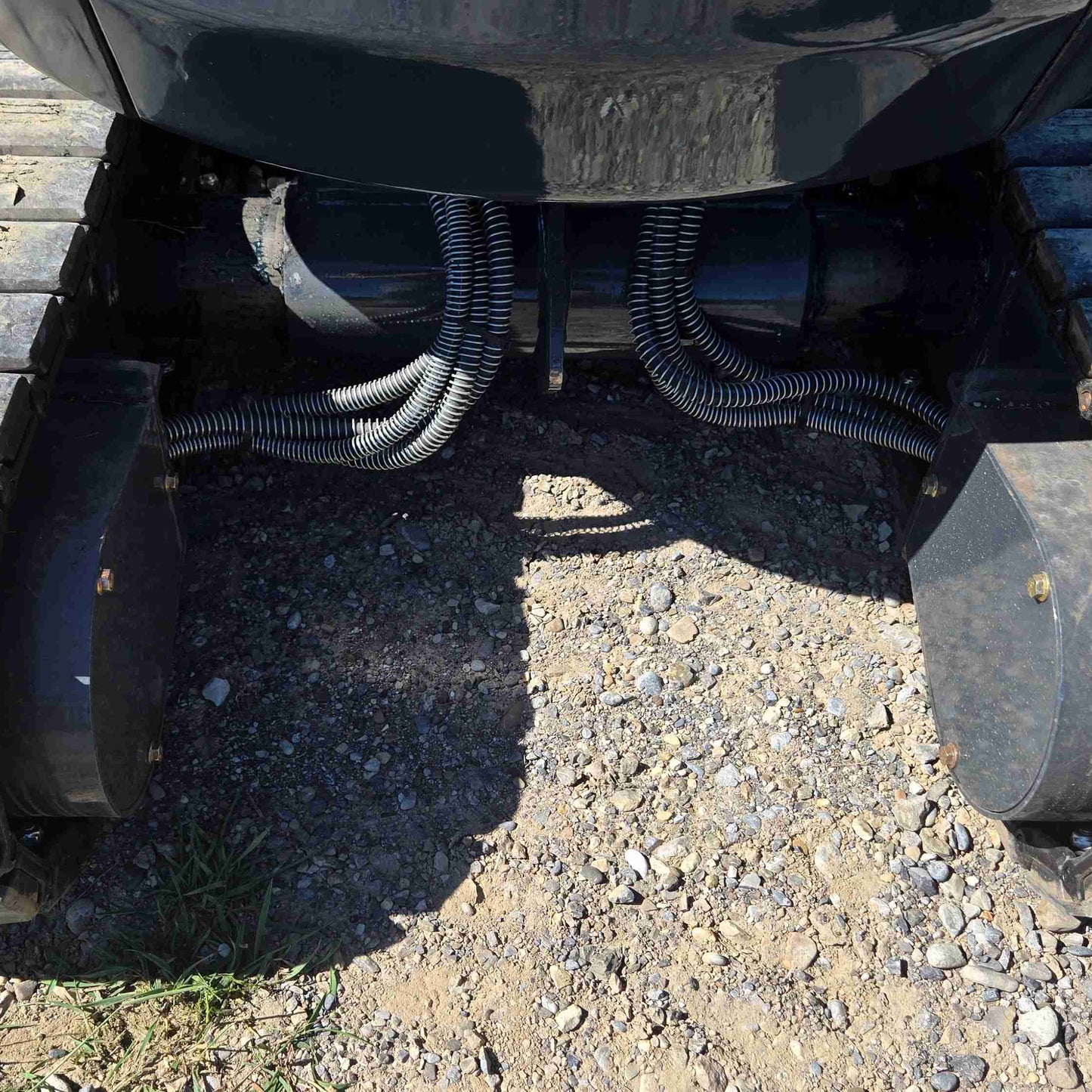 Close-up view of JoyT5 mini excavator undercarriage showing protected hydraulic hose and cable routing between rubber tracks, designed for durability, smooth operation and long service life in construction and landscaping jobs across Canada