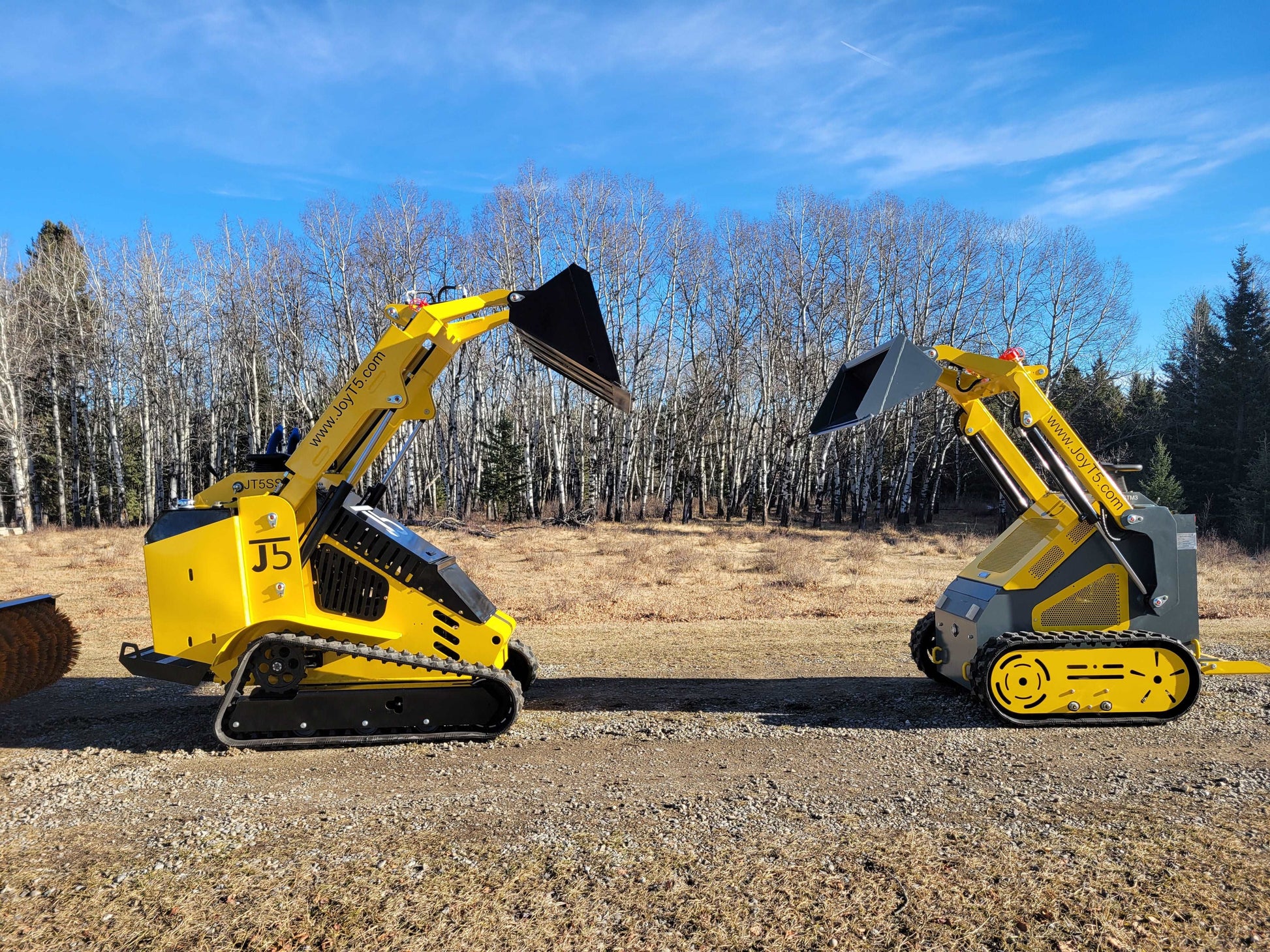 Comparison of JoyT5 mini skid steer loaders with rubber tracks and wheels, buckets raised in outdoor setting.