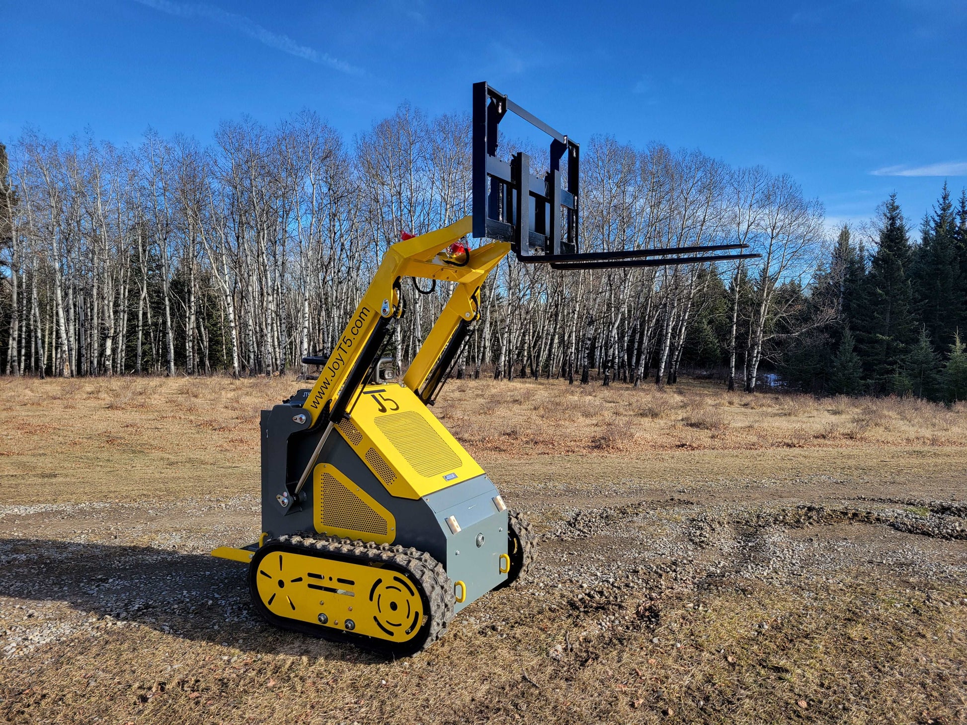 JoyT5 mini skid steer loader lifting pallet fork attachment on rough outdoor terrain