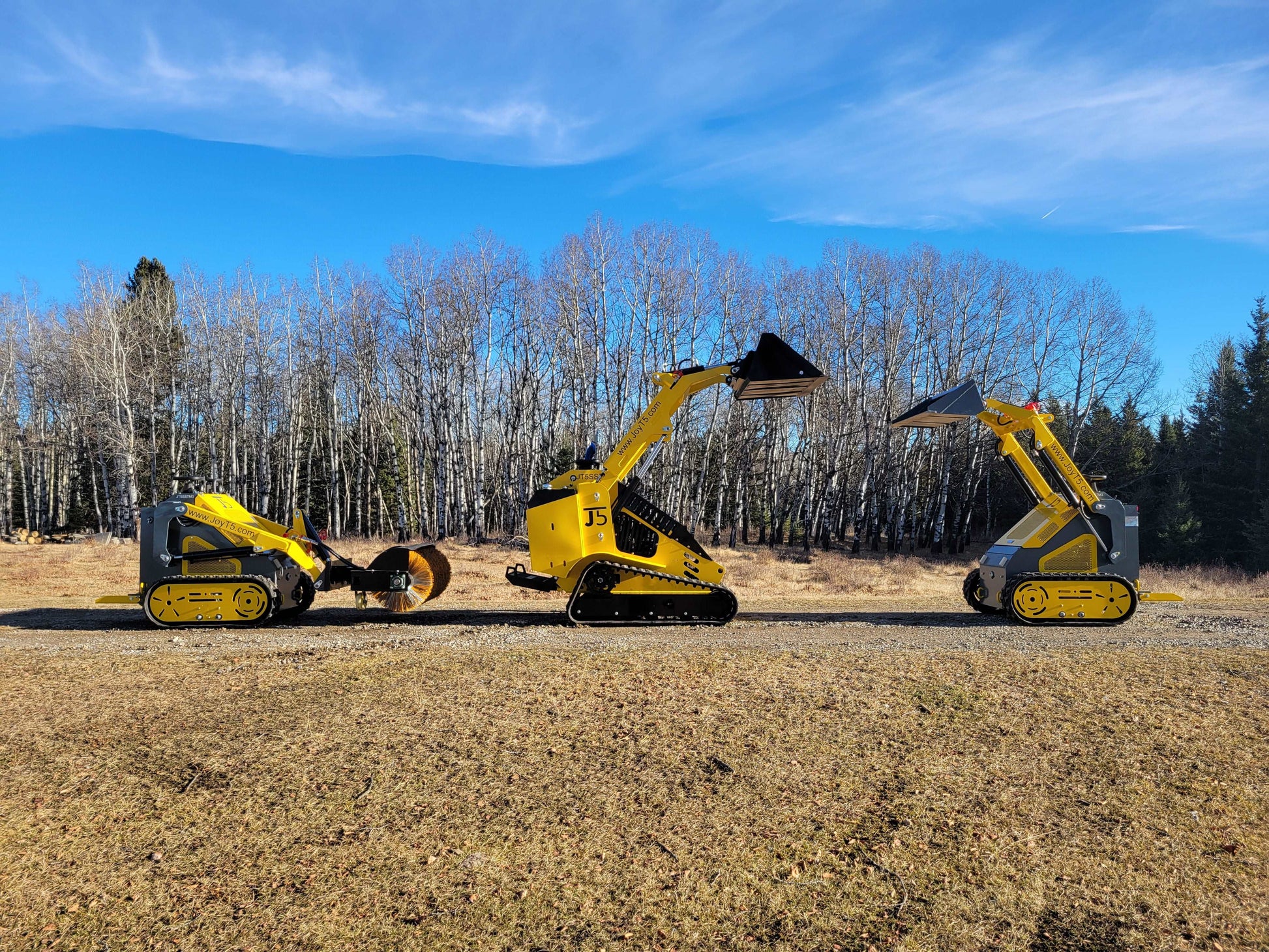 Three JoyT5 mini skid steer loaders side by side with buckets and a sweeper attachment, showcasing tracked and wheeled models outdoors.