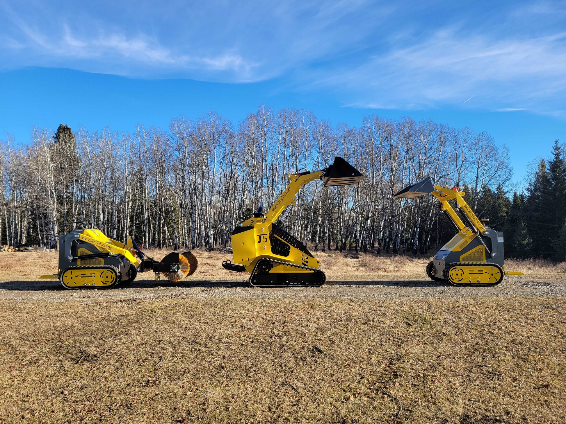 Three JoyT5 mini skid steer loaders, track and wheel versions, lined up outdoors with raised attachments.