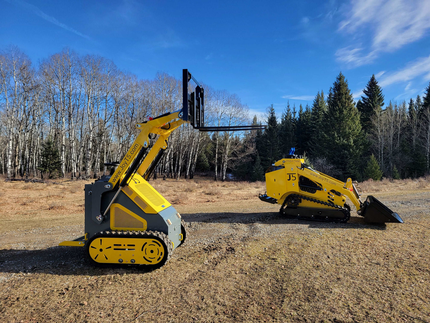 JoyT5 mini skid steer loaders, one with pallet fork attachment and another with bucket attachment, working outdoors