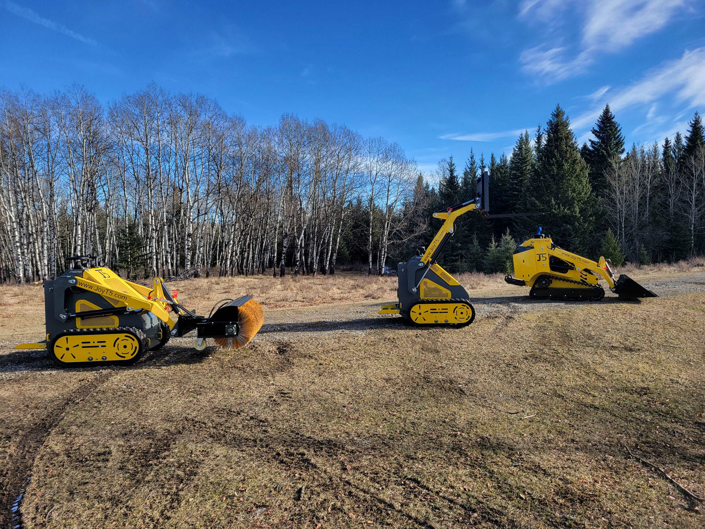 Three JoyT5 mini skid steer loaders outdoors, equipped with sweeper, pallet fork, and bucket attachments