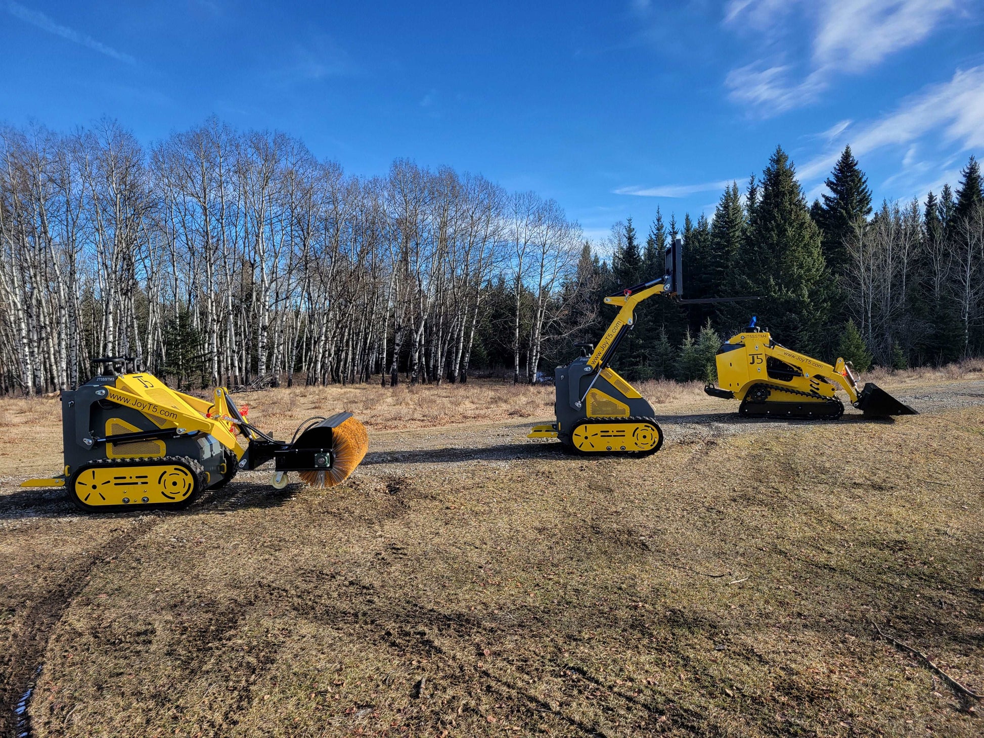 Three JoyT5 mini skid steer loaders outdoors, equipped with sweeper, pallet fork, and bucket attachments
