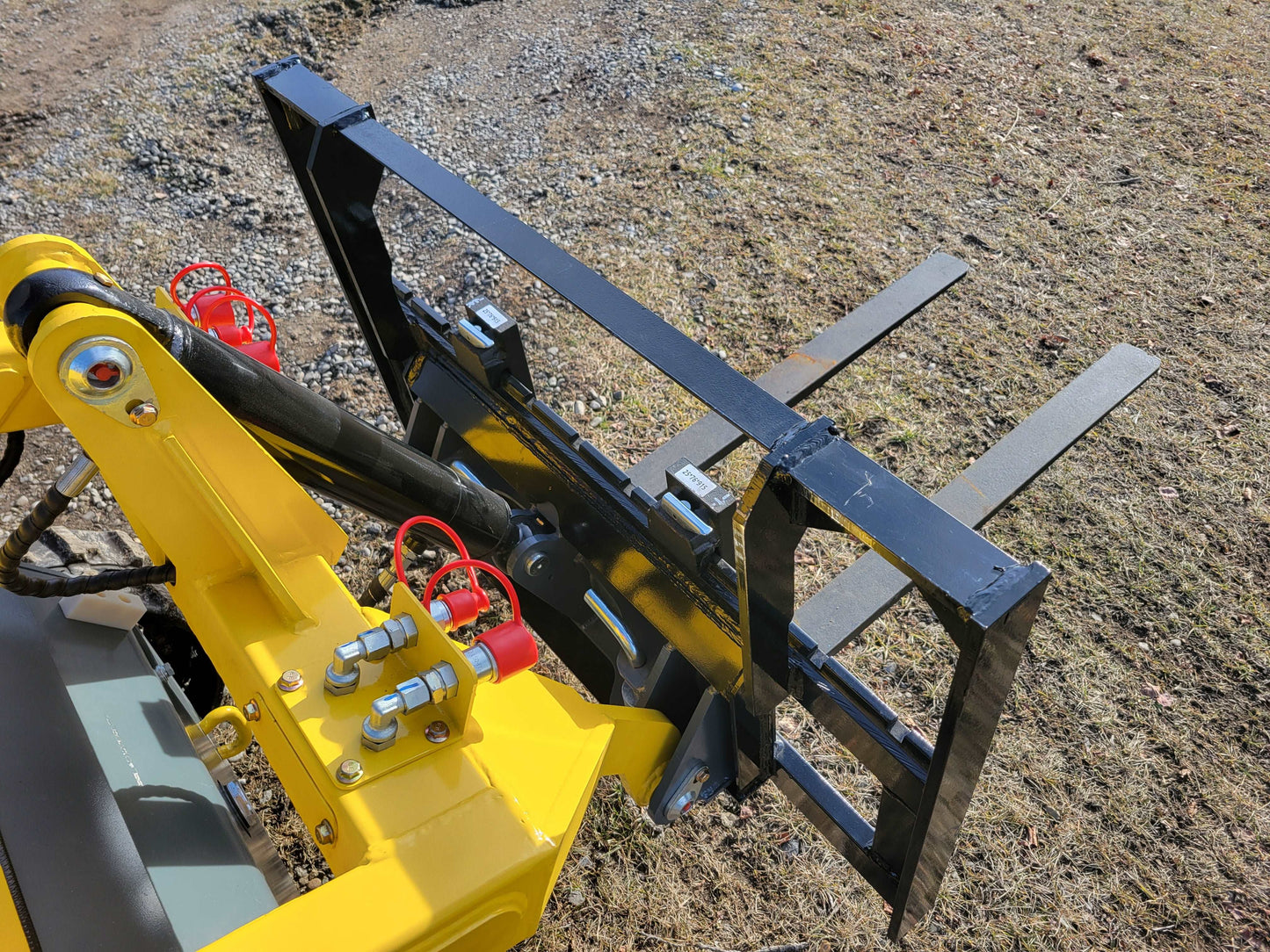 JoyT5 mini skid steer pallet fork attachment with hydraulic couplers and steel forks shown in a Canada outdoor worksite
