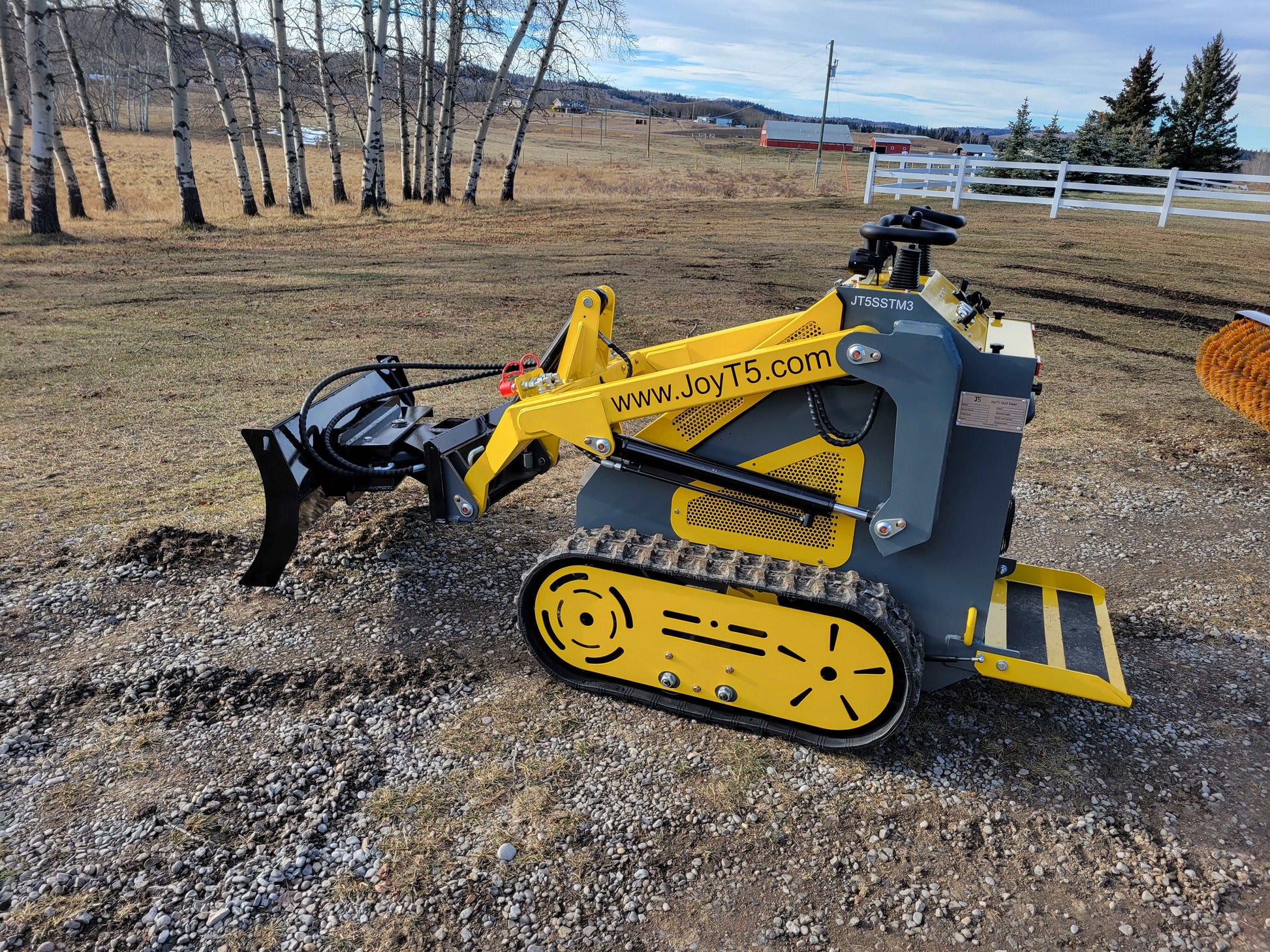 JoyT5 mini skid steer side view with ripper attachment working at a Canada outdoor site