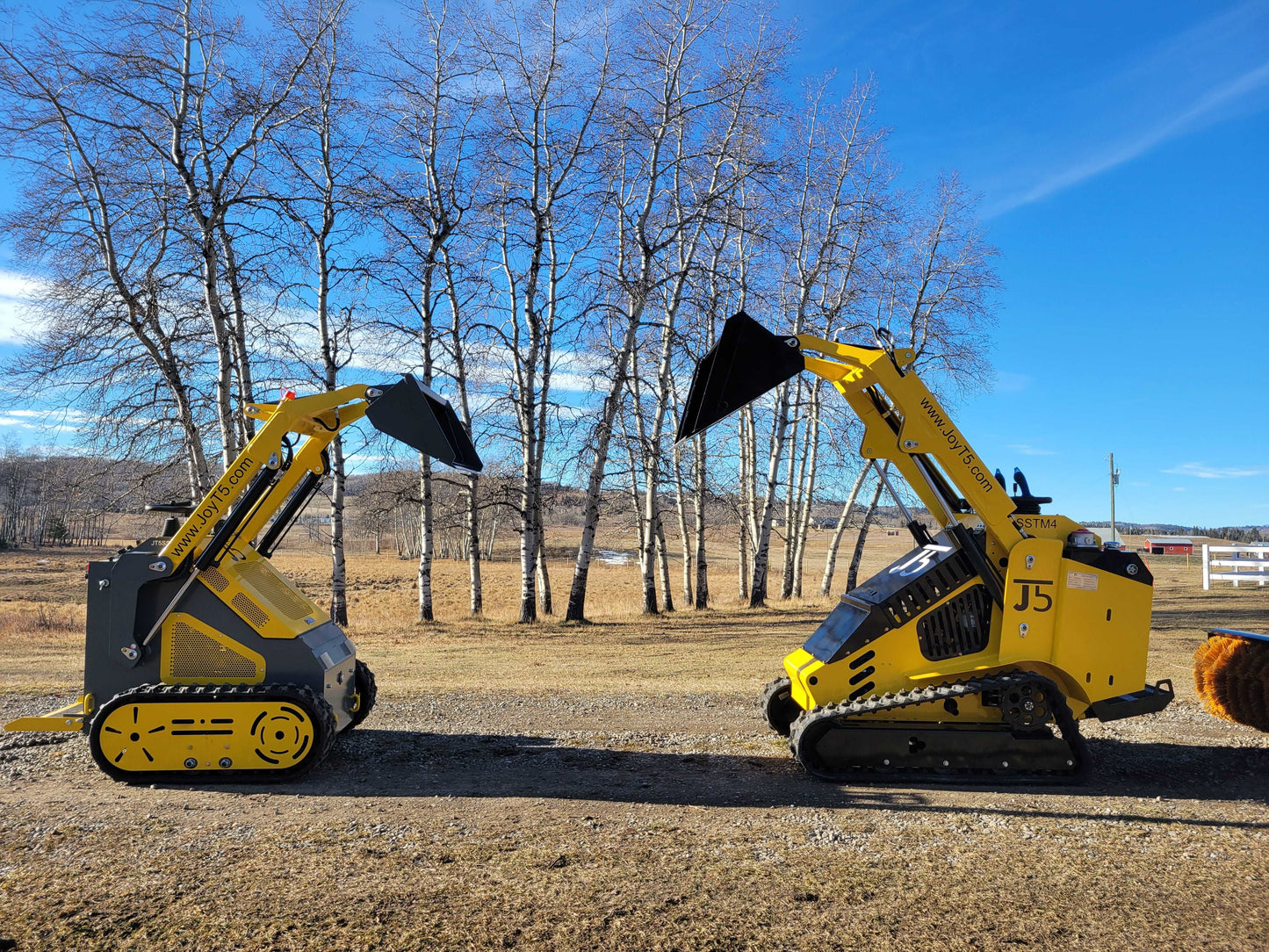 Two JoyT5 mini skid steer loaders side by side showing track vs wheel configurations on a sunny day.