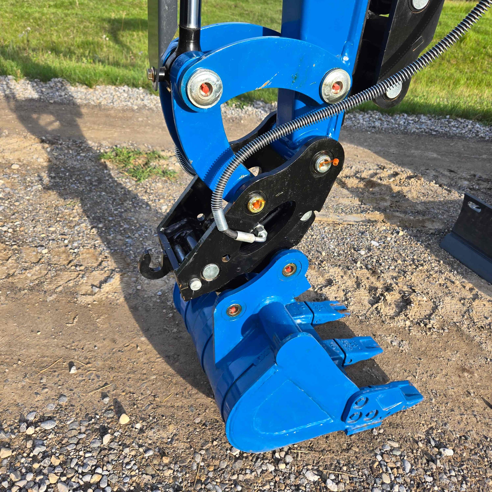 Close-up view of JoyT5 Rippa R18 Mini Excavator digging bucket with sharp teeth, hydraulic connectors, and joint assembly on gravel surface