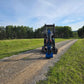 Front view of JoyT5 Rippa R18 Mini Excavator on gravel road with green grass and forest background