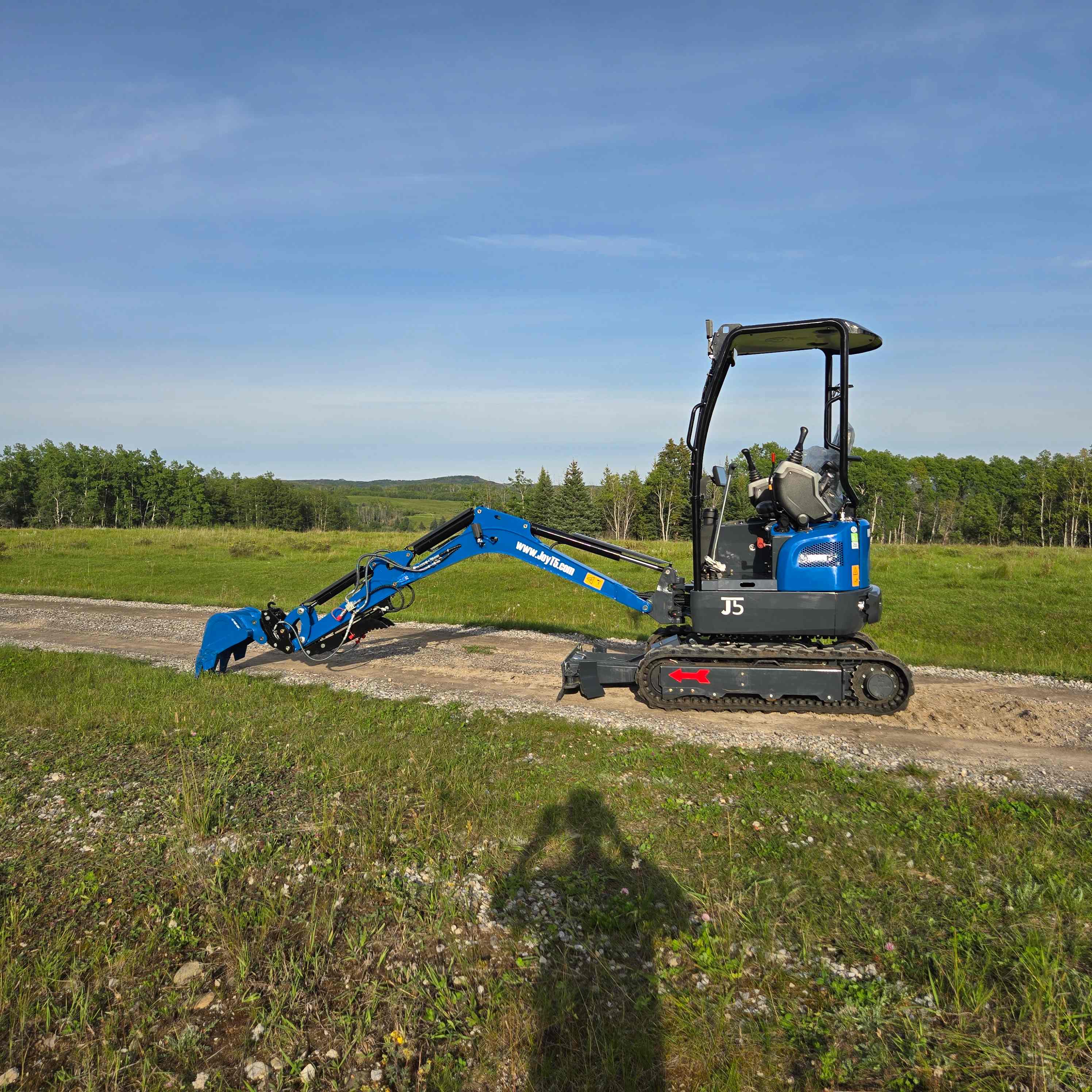 JoyT5 Rippa R18 Mini Excavator side view with arm lowered working on dirt road in rural landscape