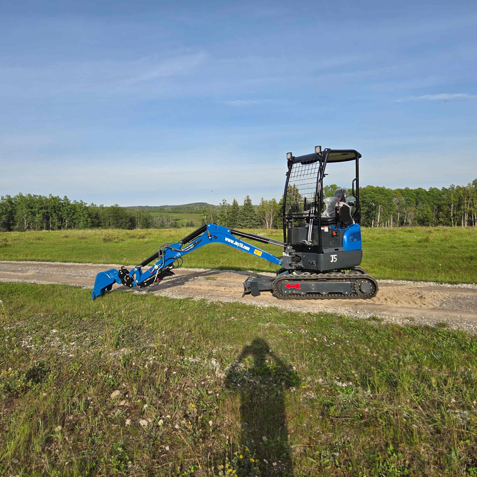 JoyT5 Rippa R18 Mini Excavator side view with arm lowered working on dirt road in rural landscape