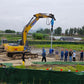 JT5 anchor drive mounted on XCMG XE210 excavator performing helical pile installation with construction workers at a foundation project site