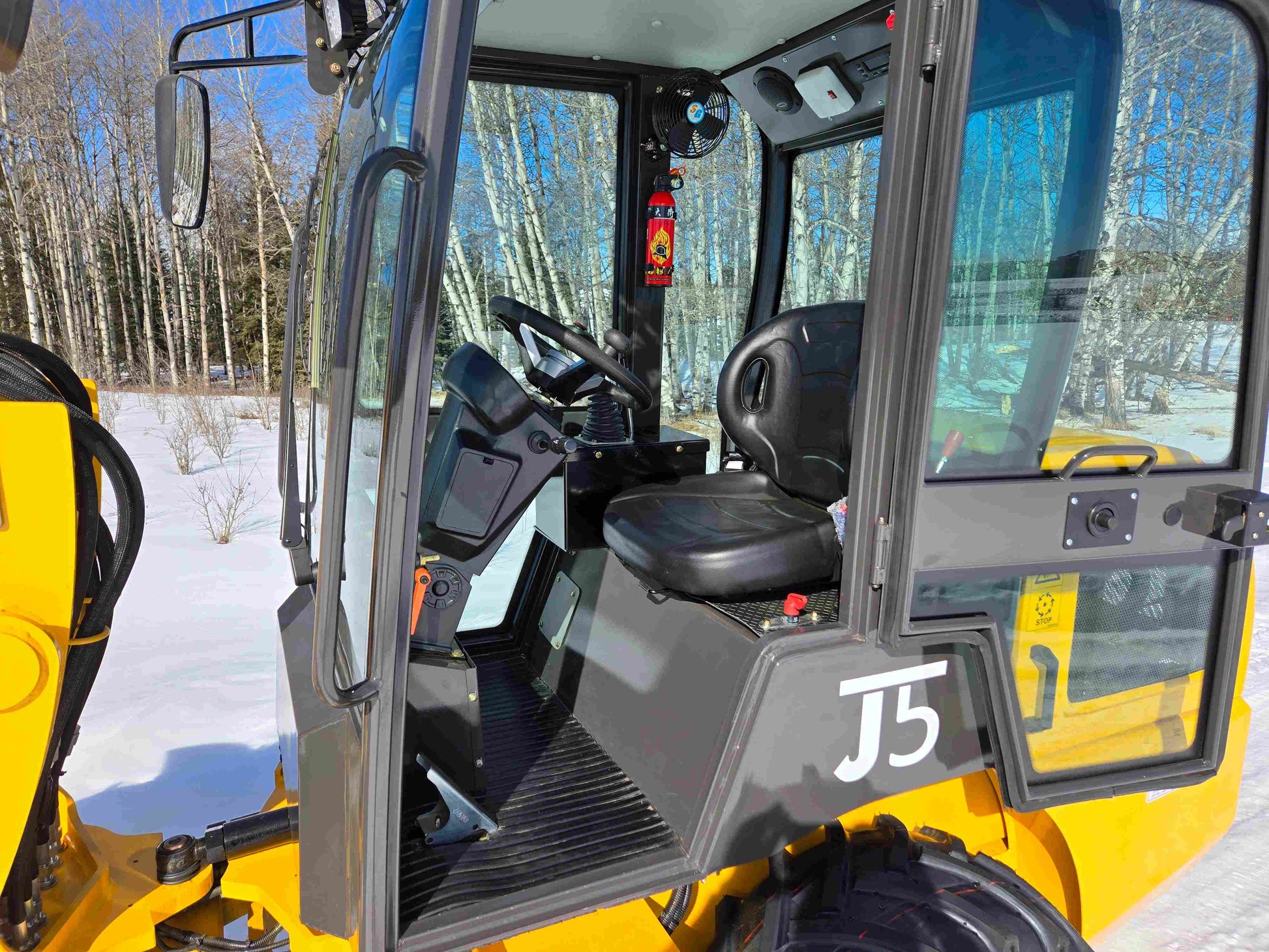 JT5 wheel loader cabin interior showing driver seat, steering wheel, joystick controls, and safety equipment.