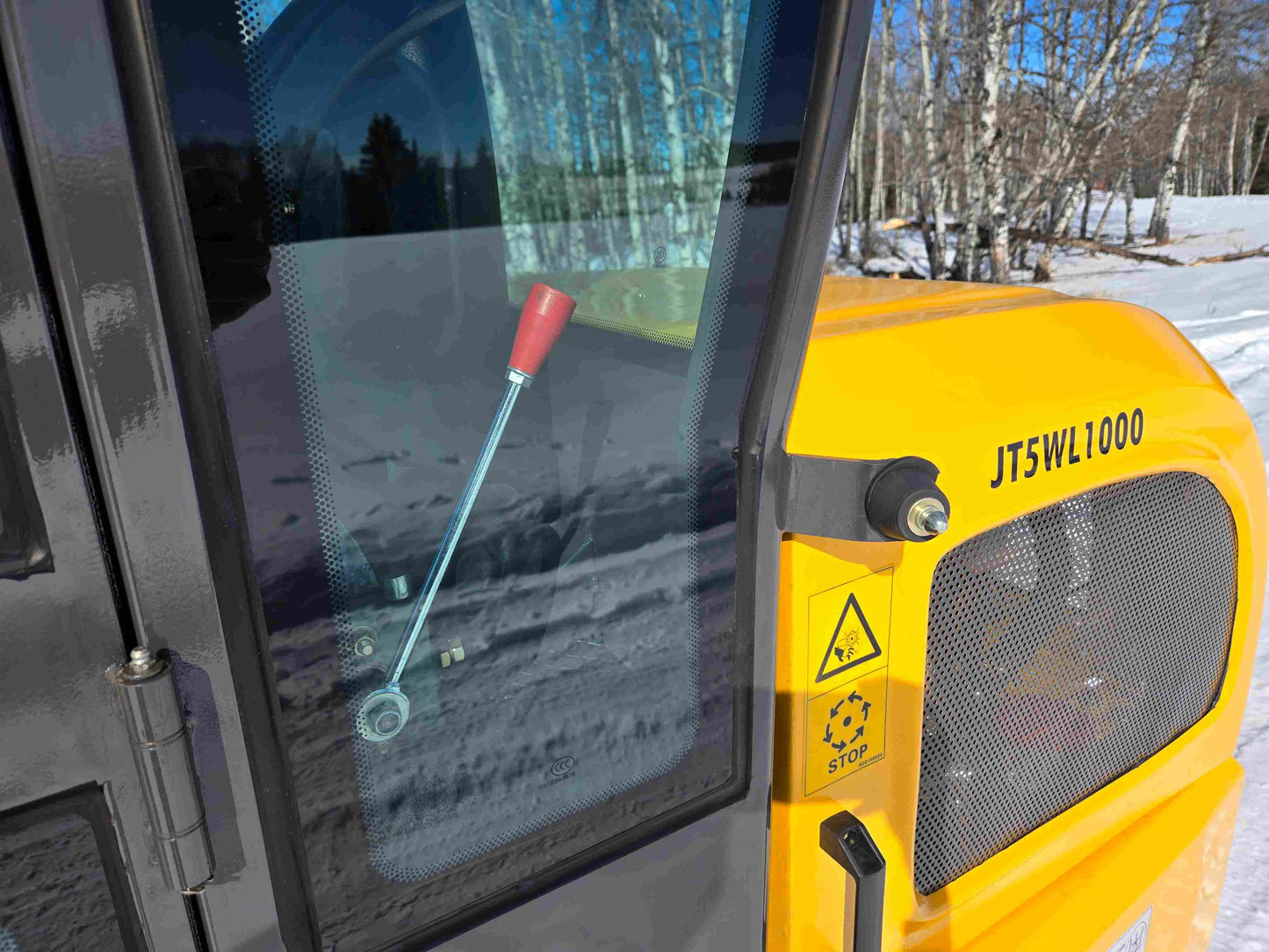 JT5WL1000 wheel loader side panel with ventilation grill, safety warning label, and red control handle visible through cabin glass.