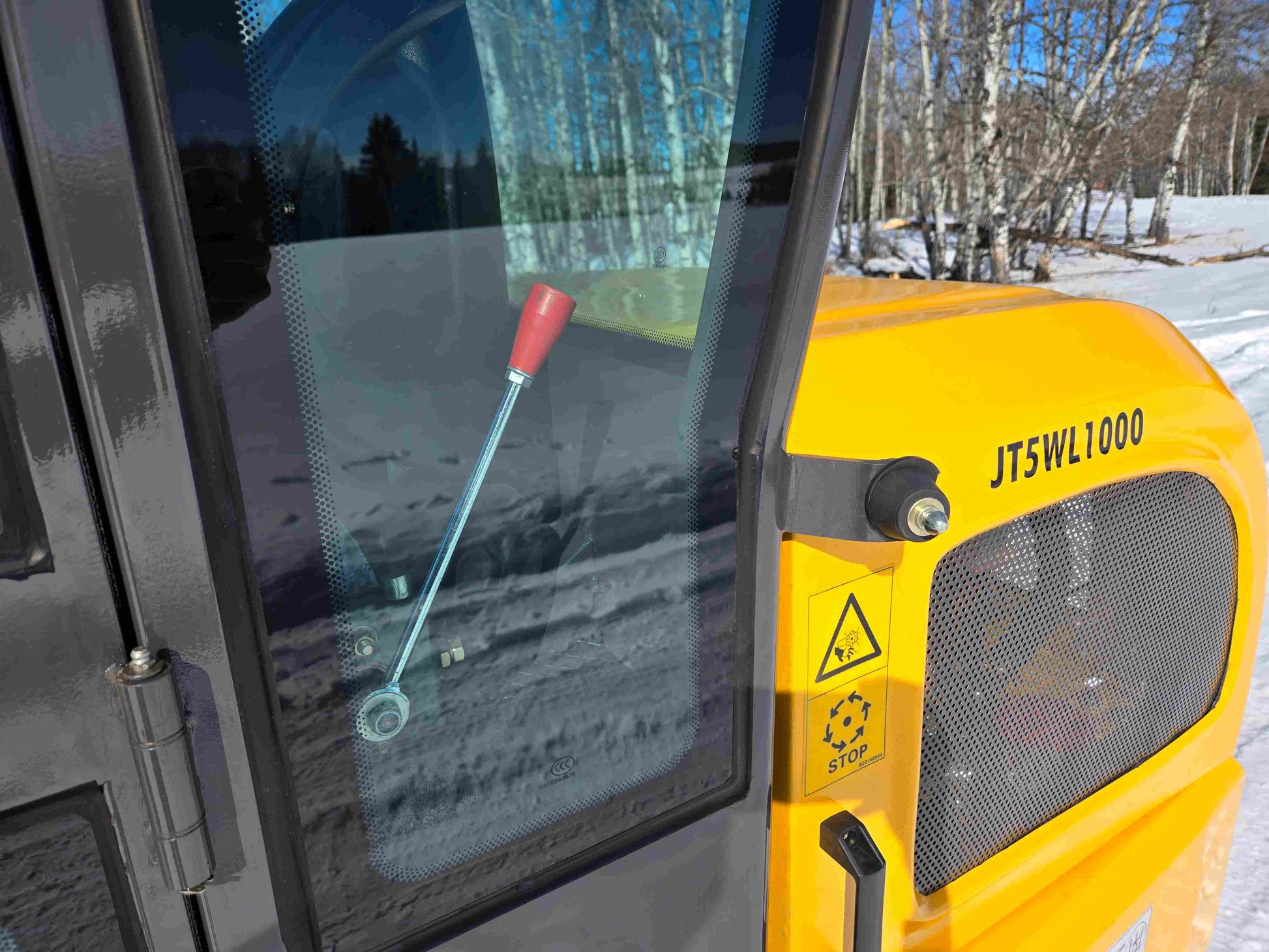 JT5WL1000 wheel loader side panel with ventilation grill, safety warning label, and red control handle visible through cabin glass.