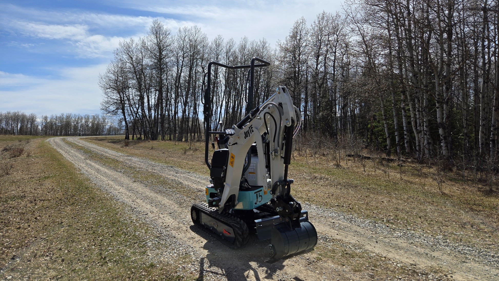 JT5120P 1.2 ton mini excavator driving along gravel road near forest showing zero tail compact design for small construction projects in Canada with JoyT5 support
