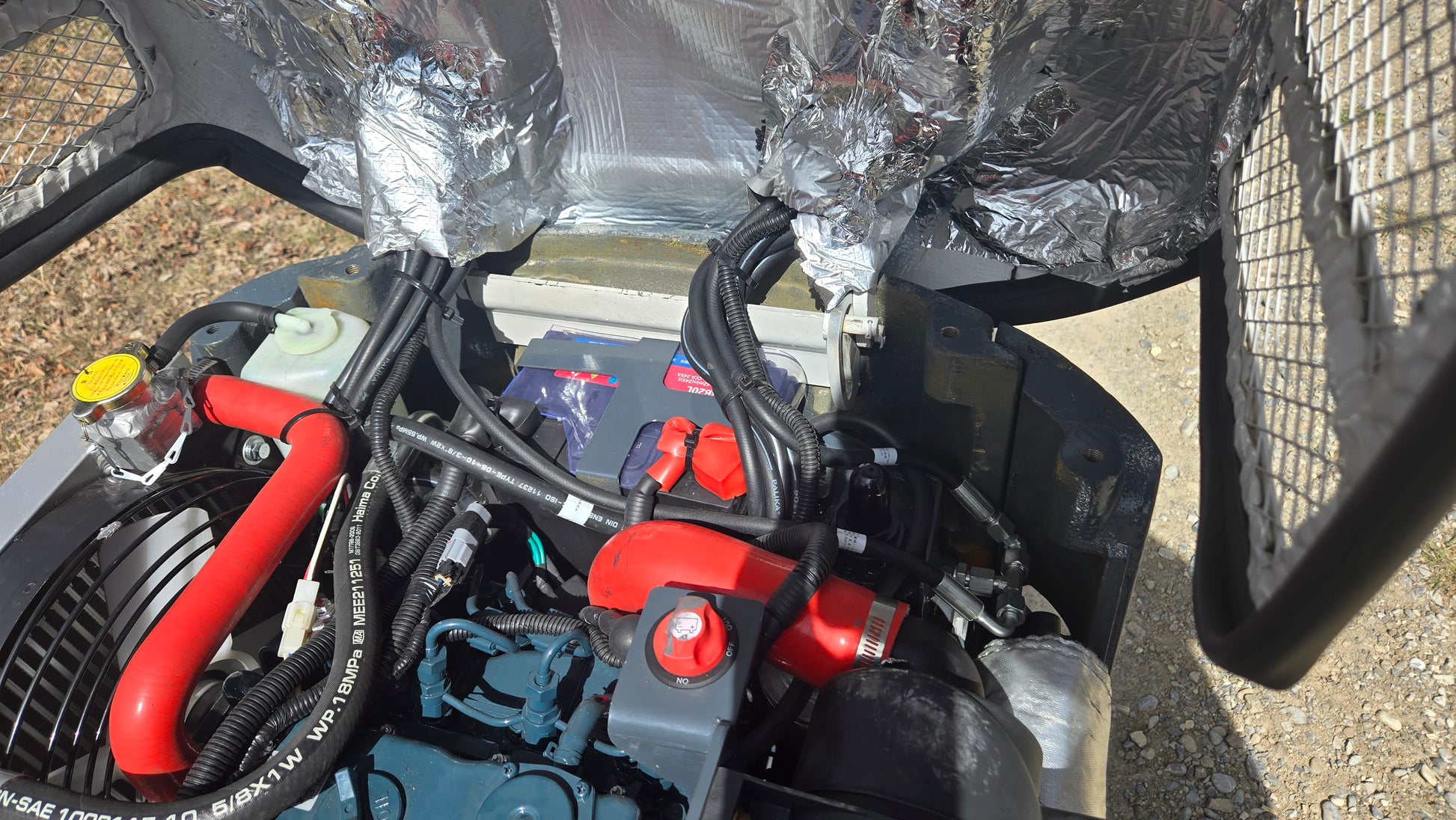 Close-up view of JT5120P mini excavator diesel engine with battery, radiator, and wiring components visible.
