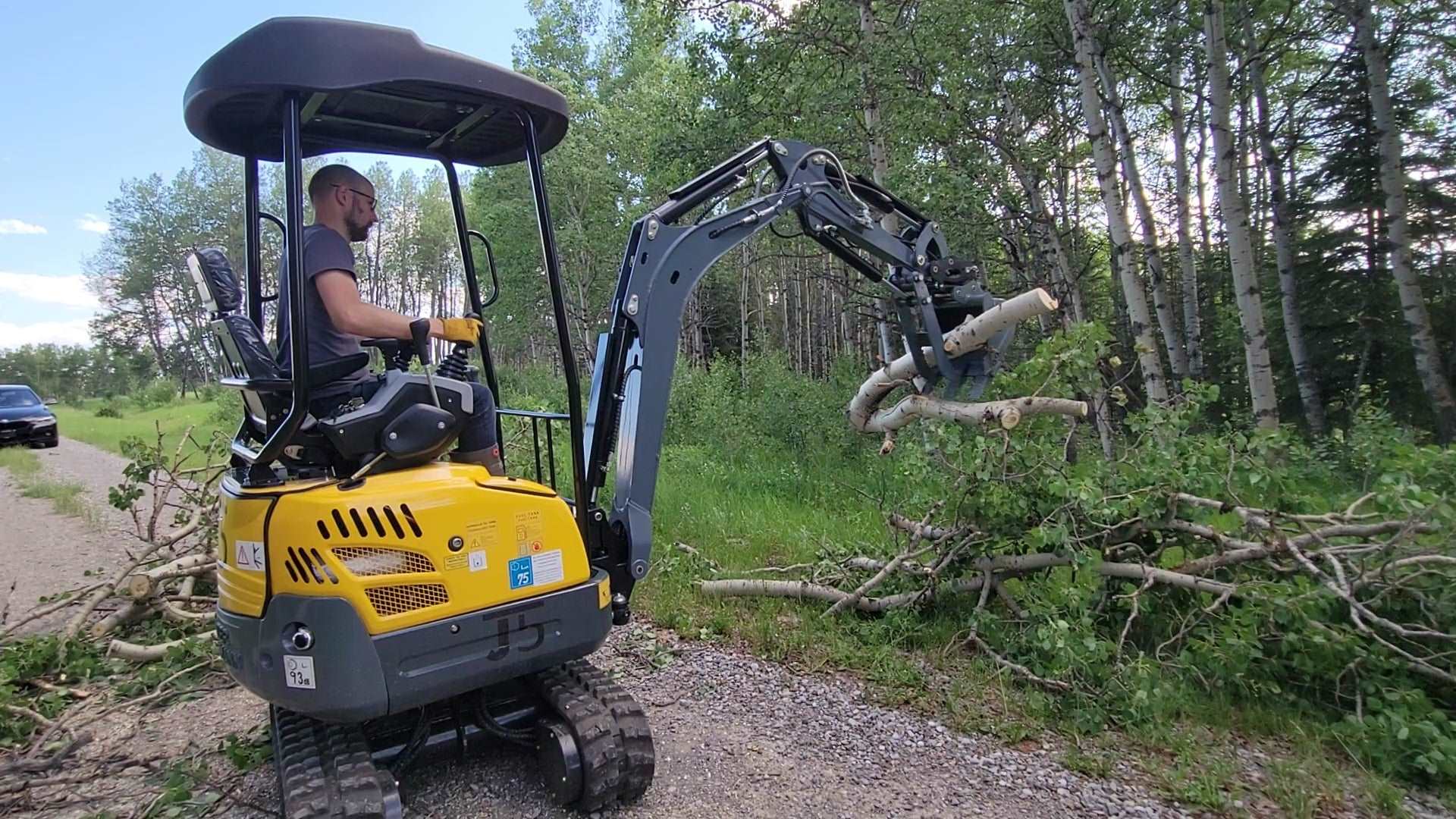 JoyT5 JT5200 2 ton mini excavator with Kubota D902 engine lifting logs using hydraulic thumb. Compact zero-tail digger with U-boom, side swing boom, and extendable undercarriage for construction and landscaping.
