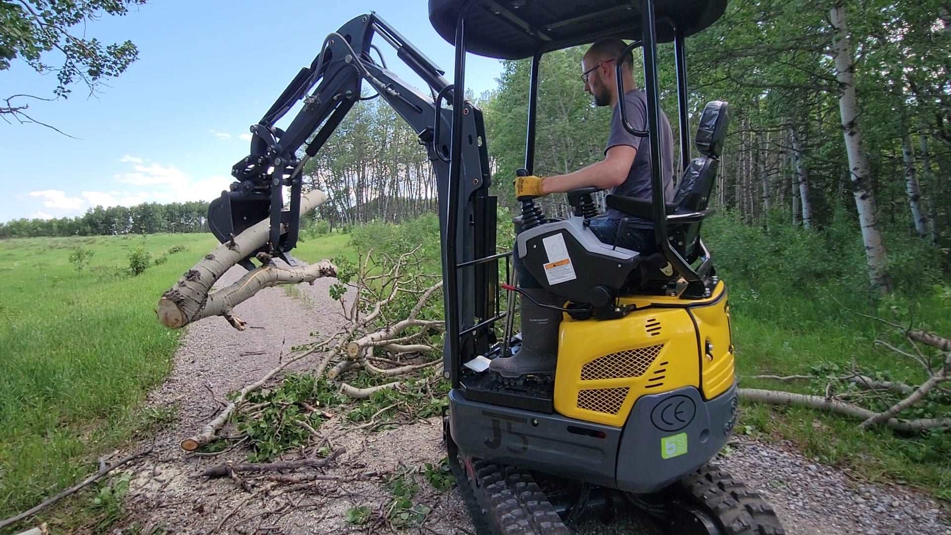 JoyT5 JT5200 2 ton mini excavator with Kubota D902 engine lifting heavy tree branches using hydraulic thumb. Compact zero-tail digger with U-boom and side swing boom for construction and landscaping.
