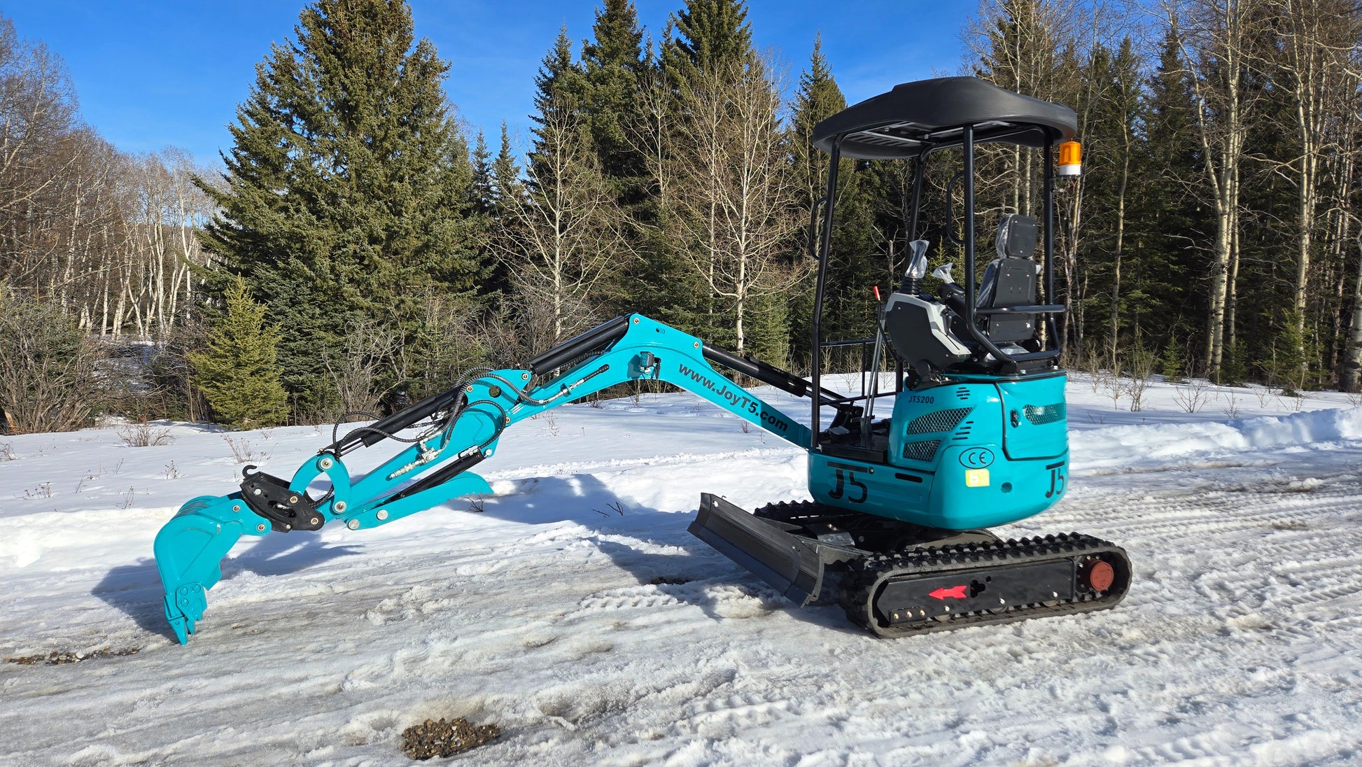 Rear side view of JoyT5 JT5200 2 ton mini excavator with boom extended forward and dozer blade lowered. Compact Kubota-powered digger with zero-tail swing and hydraulic thumb for construction and landscaping.
