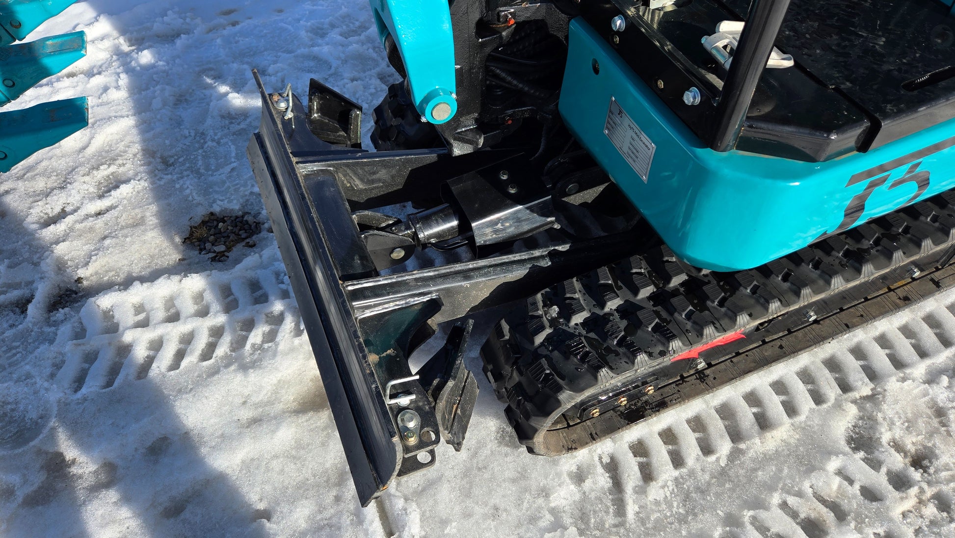 Rear side view of JoyT5 JT5200 mini excavator dozer blade and rubber track system on snow-covered ground.
