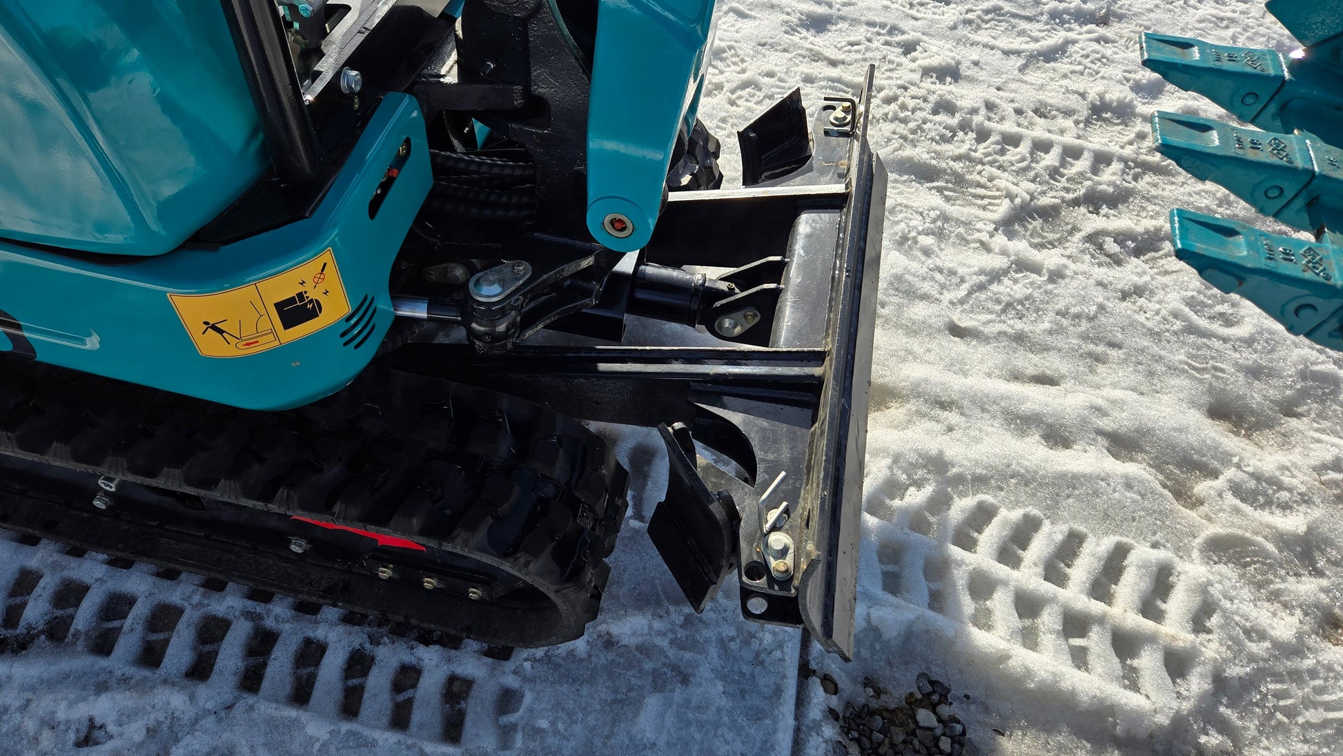 Top view of JoyT5 JT5200 mini excavator showing dozer blade, hydraulic cylinder, and rubber track system on snow.
