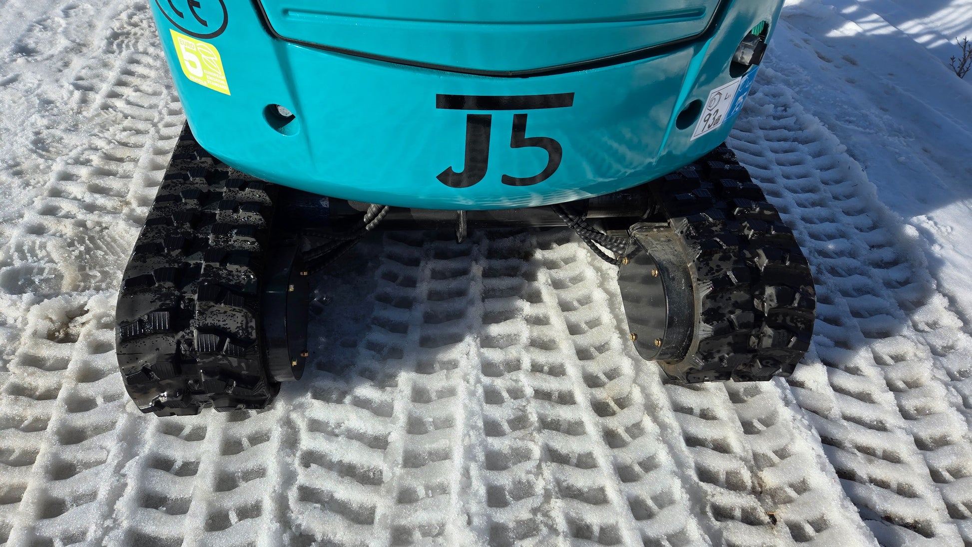 Rear counterweight and rubber tracks of JoyT5 JT5200 mini excavator parked on snow.
