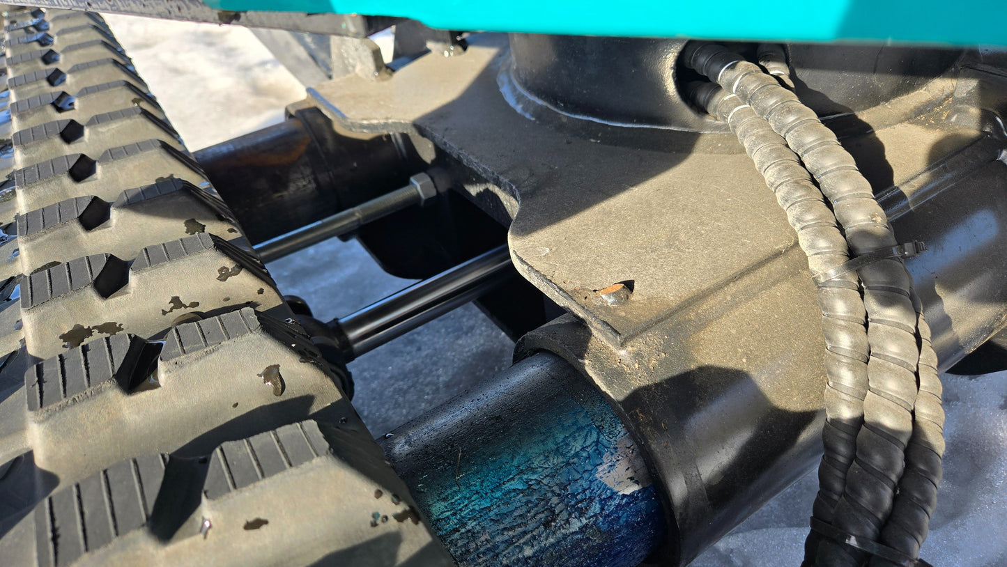 Close-up of JoyT5 JT5200 mini excavator undercarriage showing rubber track, rollers, and hydraulic connections.
