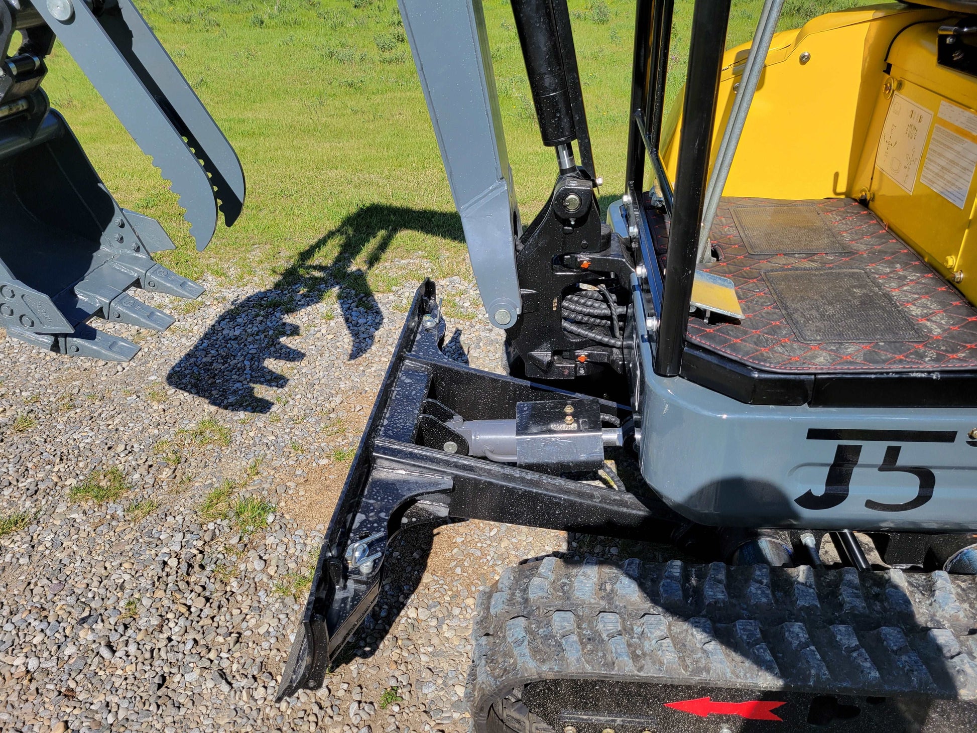 Close-up view of JT5200 mini excavator blade with hydraulic cylinder and operator floor area.
