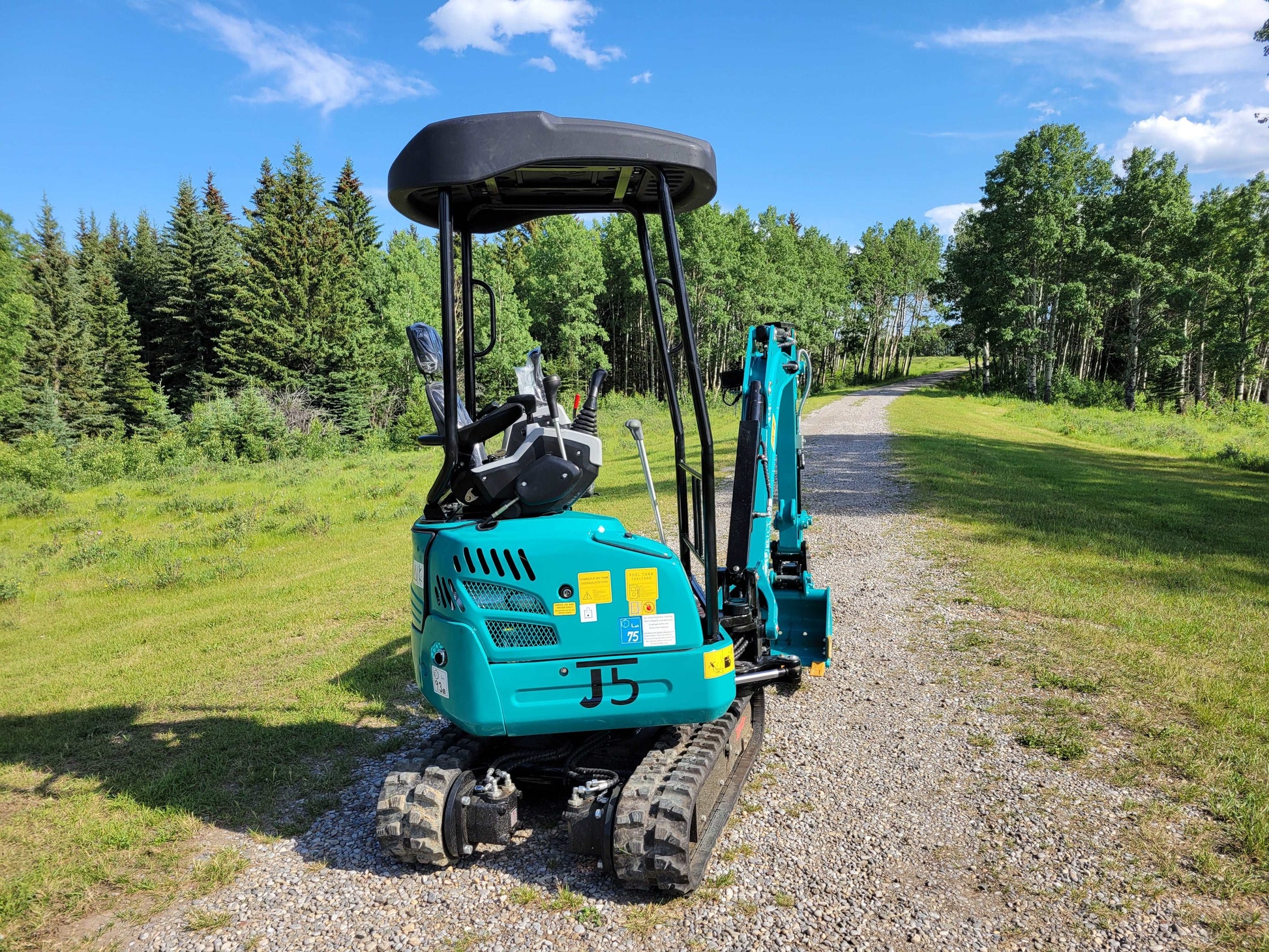 JT5200 mini excavator diagonal rear-side view showing operator cabin, rubber tracks, and digging arm on gravel path.
