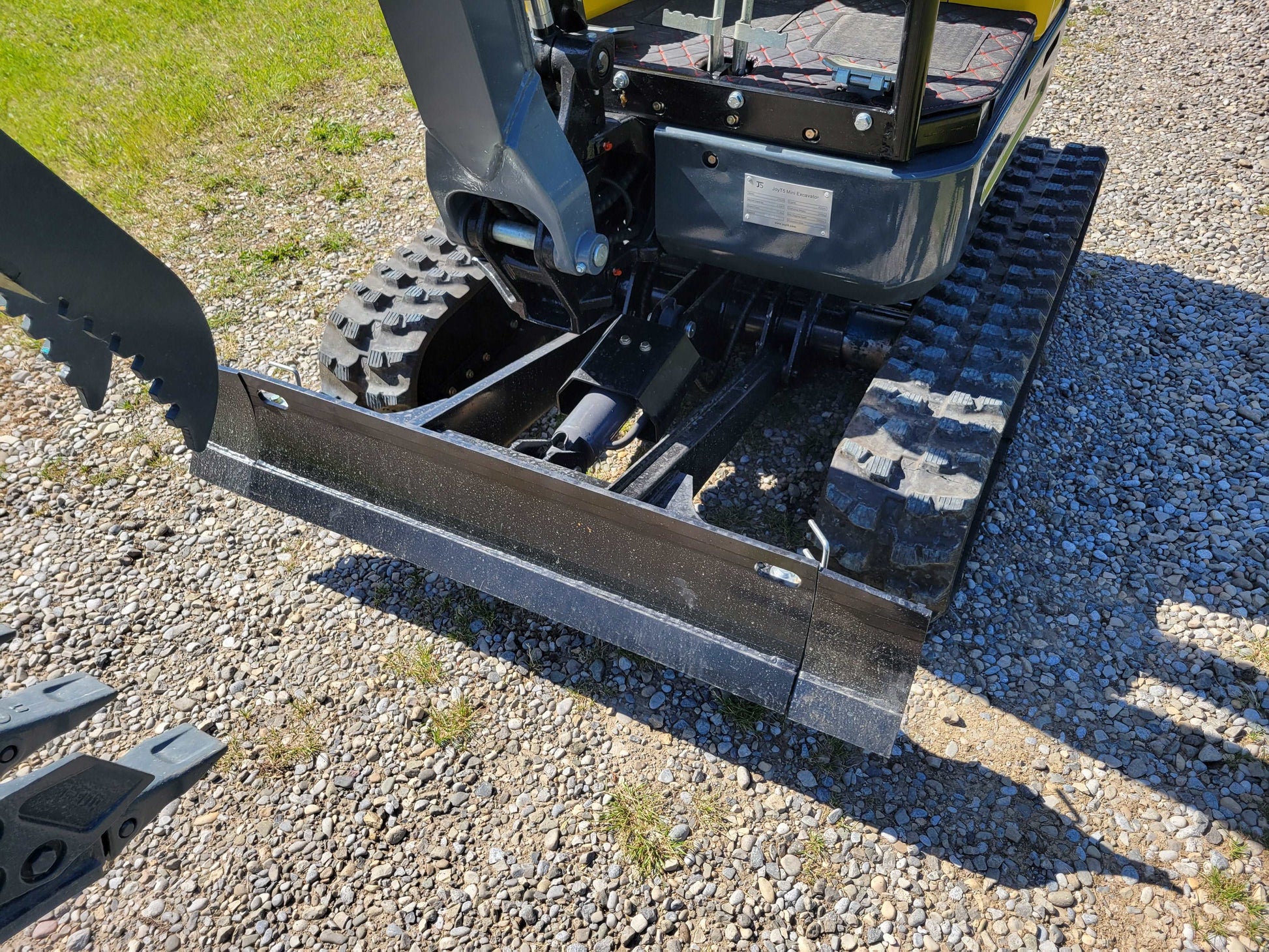 Close-up view of JT5200 mini excavator dozer blade and rubber tracks on gravel surface.
