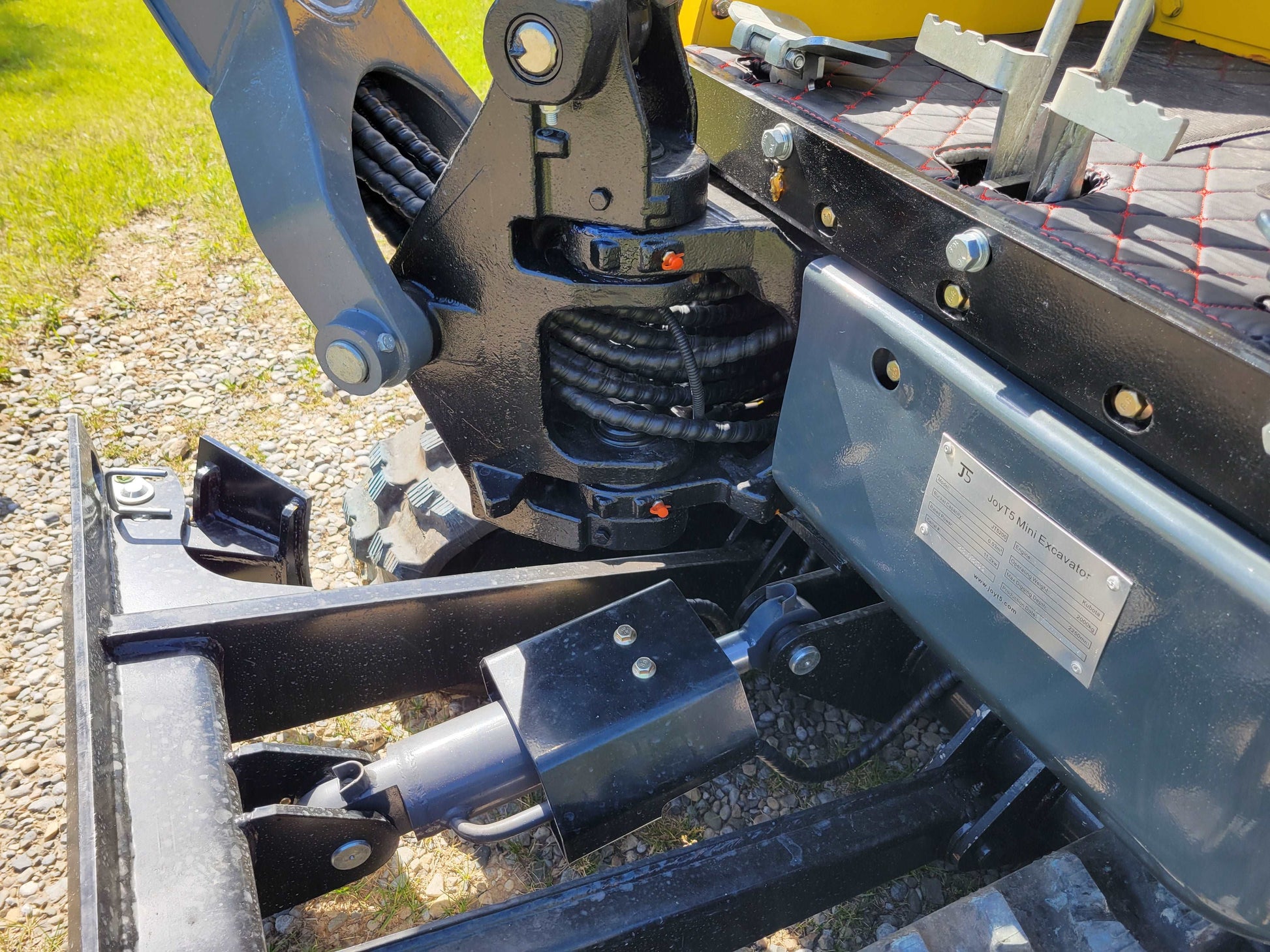 Close-up view of JoyT5 JT5200 mini excavator showing hydraulic cylinder, control levers, and specification plate.
