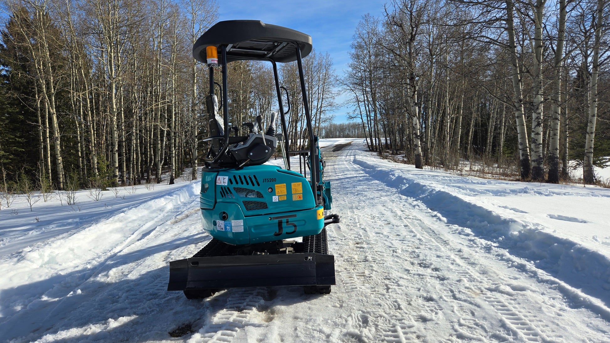 JT5200 2 ton mini excavator JoyT5 parked on snowy rural road in Canada shown from rear view surrounded by winter forest ready for landscaping and digging work
