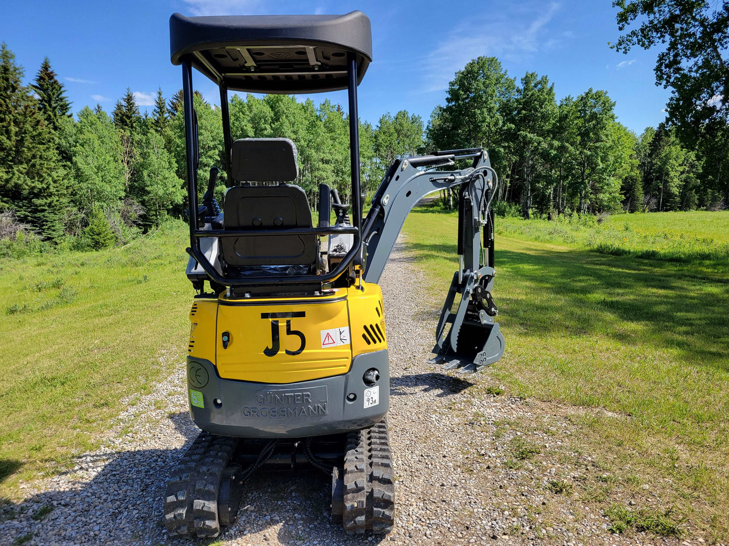 JoyT5 JT5200 mini excavator rear side view showing operator seat, canopy, rubber tracks, and digging arm with bucket.
