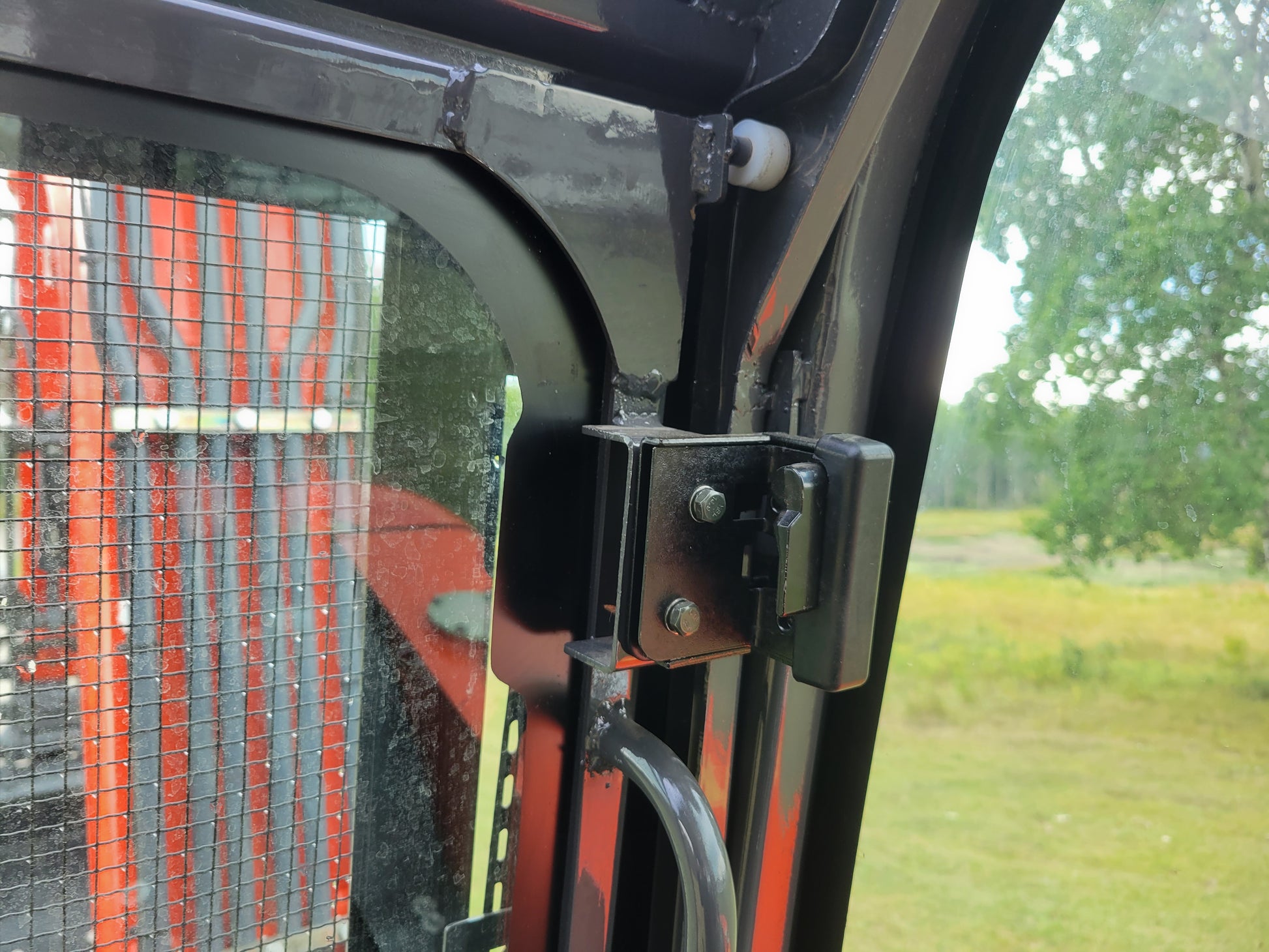 Close-up view of JT5600 mini excavator cabin door hinge mechanism with bolts and metal frame detail, showing part of window and protective mesh outside