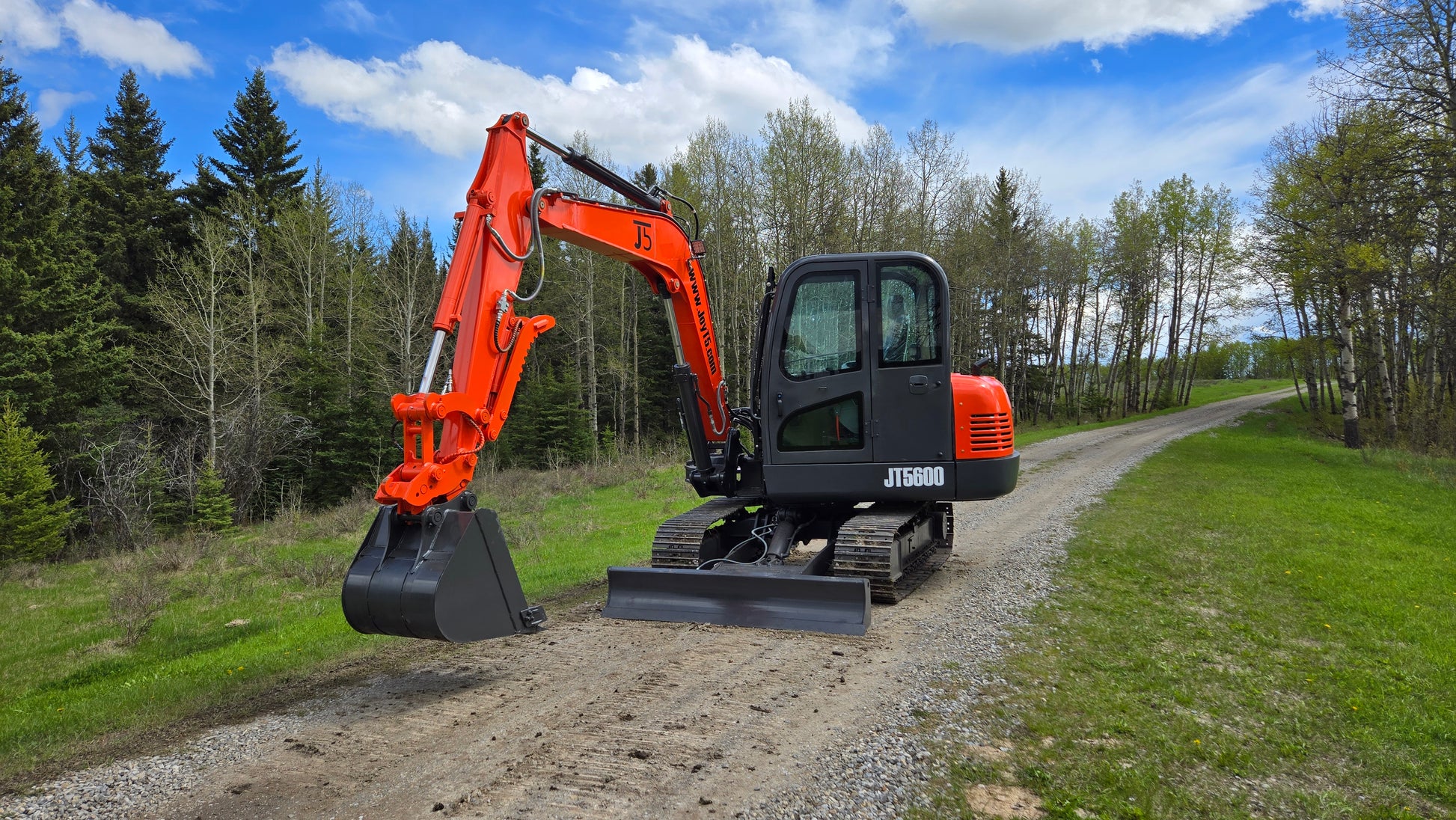 JT5600 JoyT5 6 ton mini excavator with Yanmar engine, bucket raised and dozer blade on gravel road, full cabin and hydraulic quick hitch